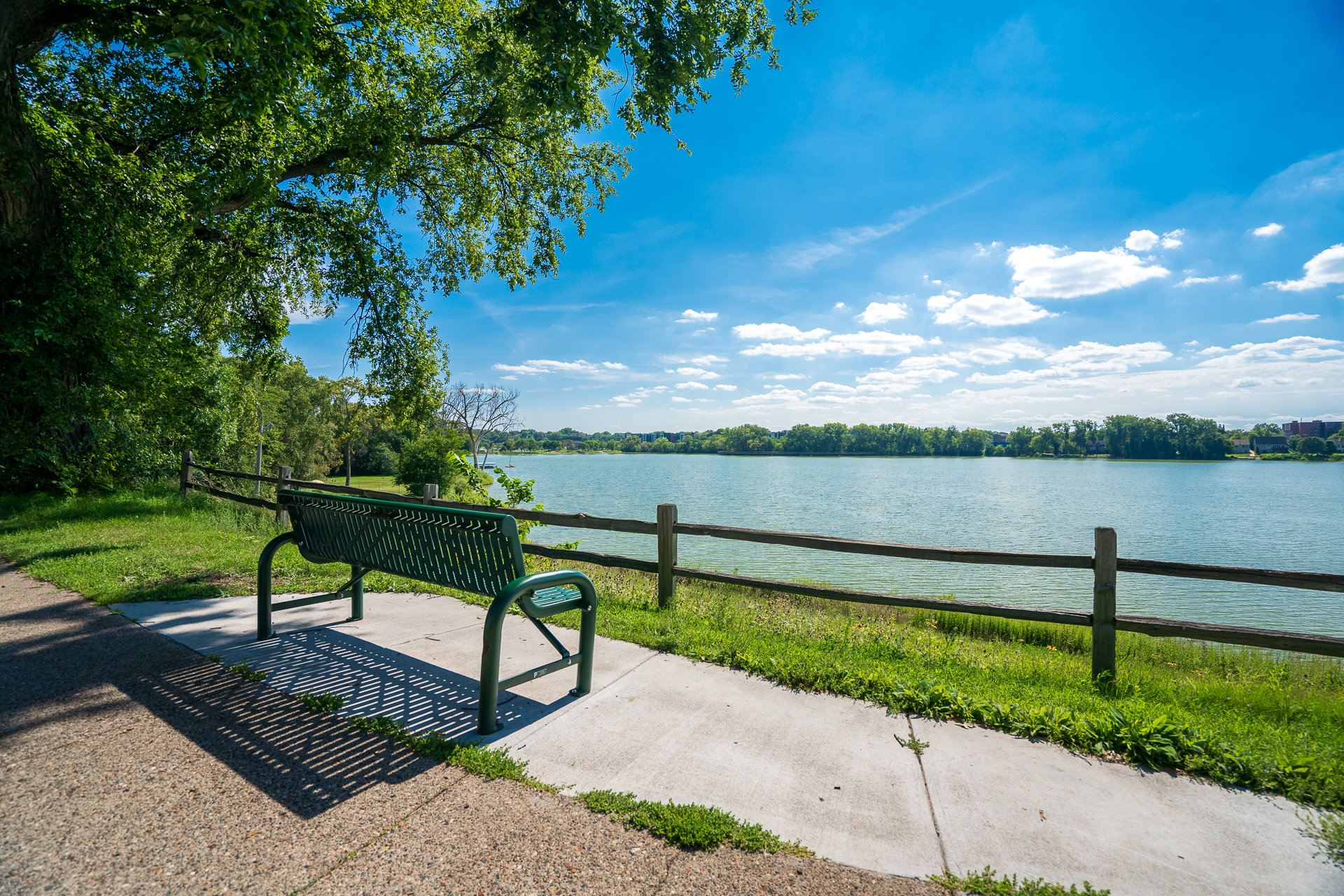 A peaceful lakeside view featuring a bench under a clear blue sky.