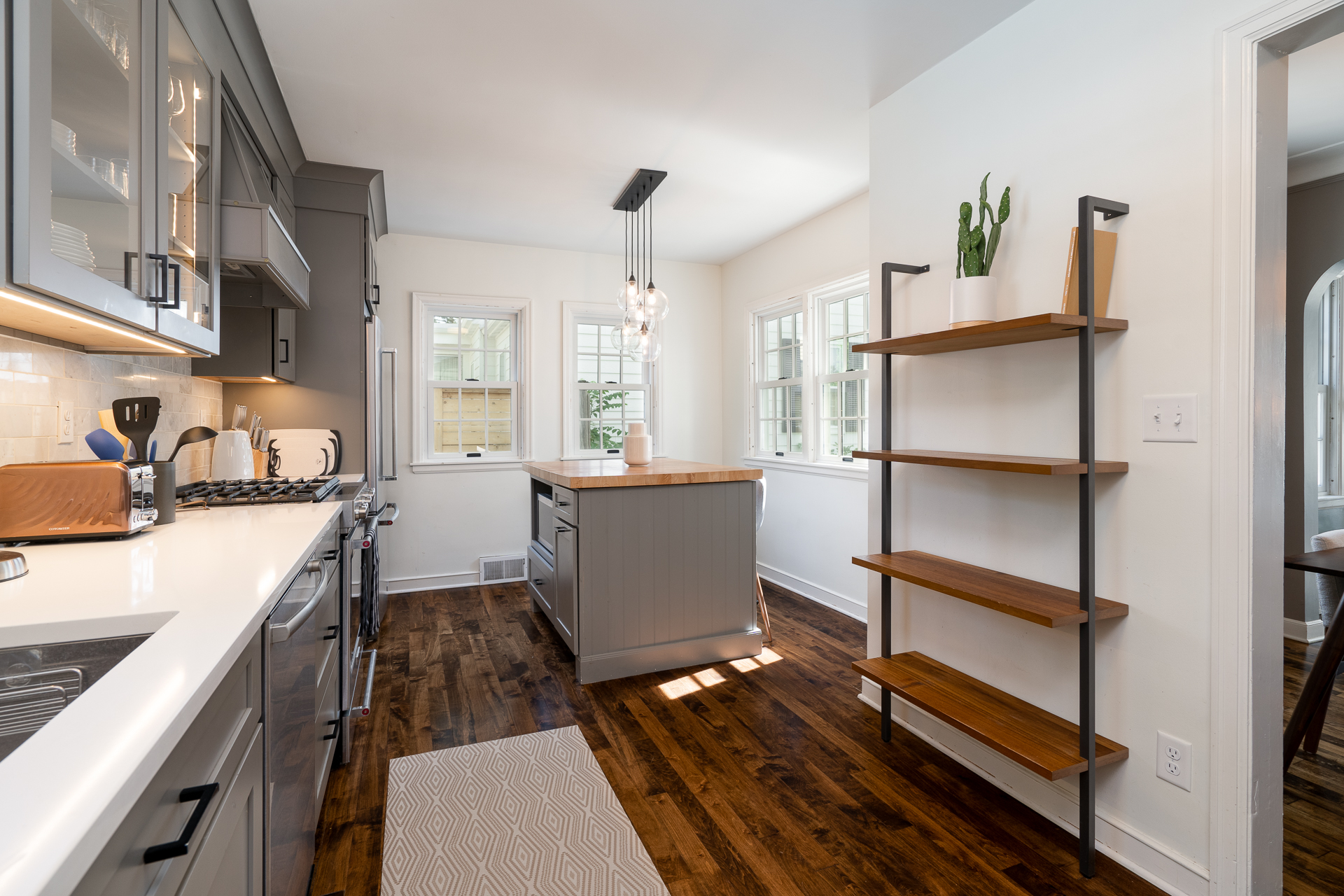 A modern kitchen with gray cabinets, a butcher block island, and stylish lighting.