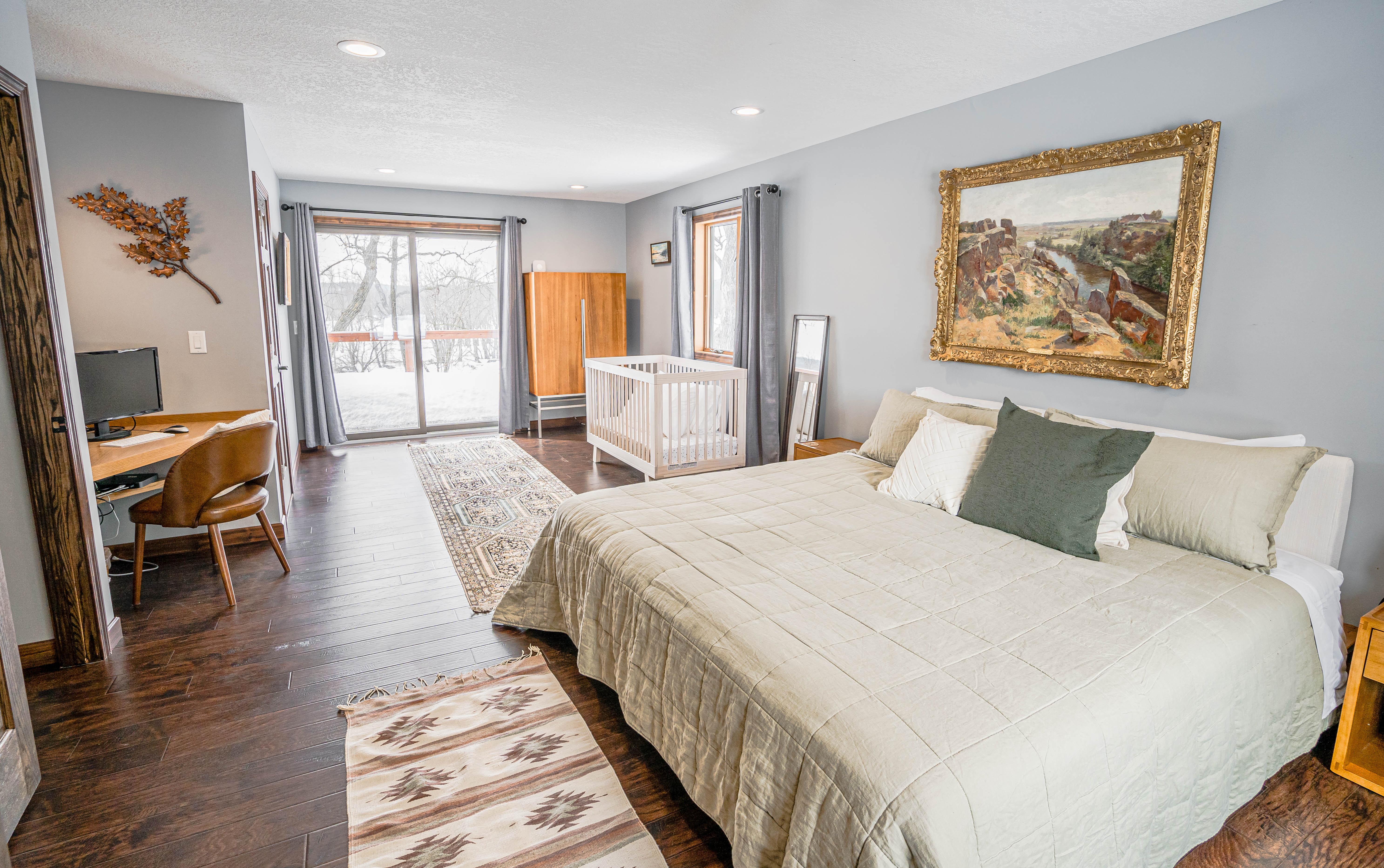 A cozy and stylish bedroom featuring a large bed, a crib, and a workspace.
