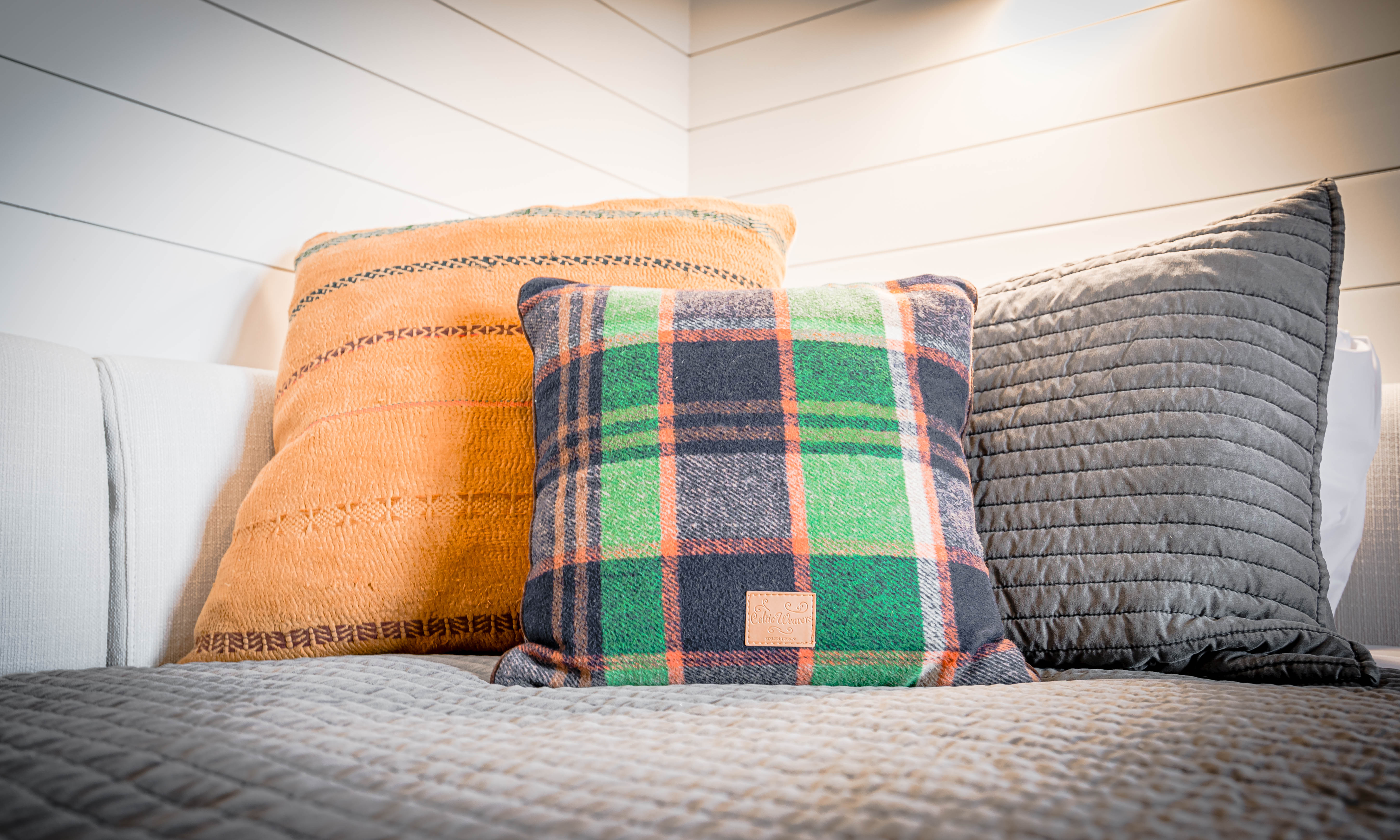 A cozy collection of decorative pillows in earthy tones and textures on a gray quilted bedspread.