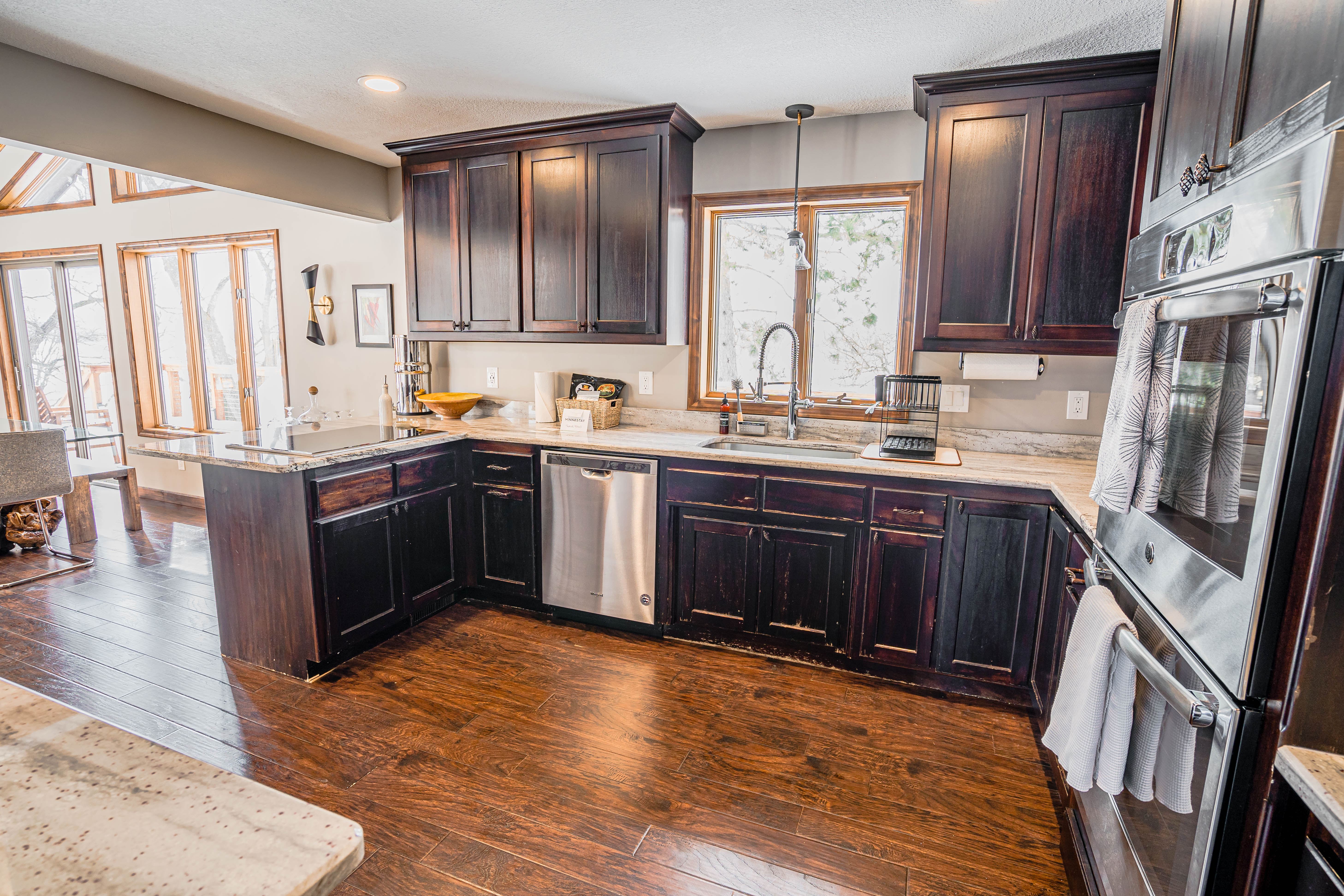 A contemporary kitchen filled with warmth and sunlight features dark wood cabinetry and elegant granite countertops.