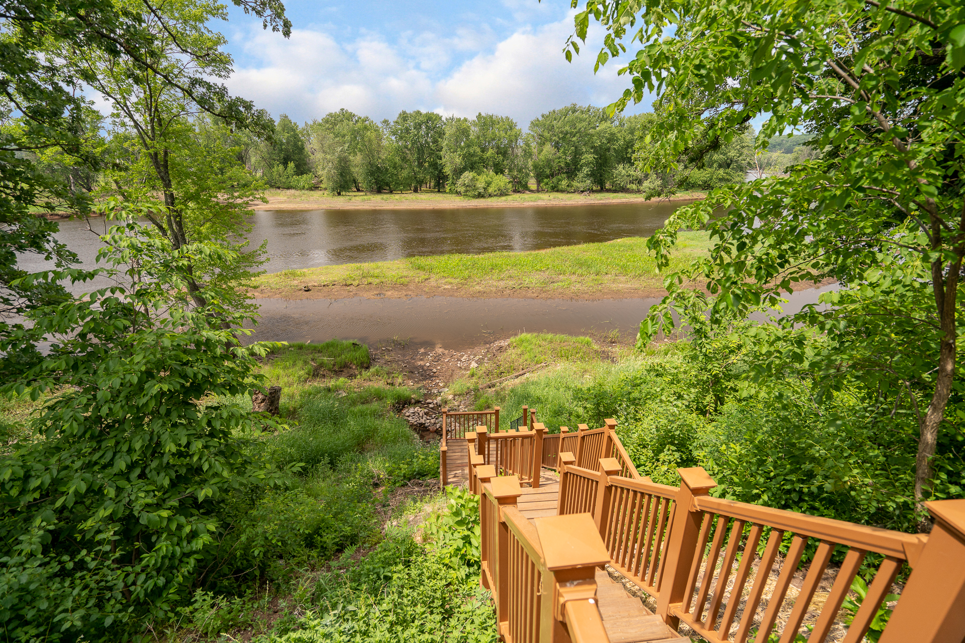 A tranquil riverside view from a wooden staircase surrounded by lush greenery.