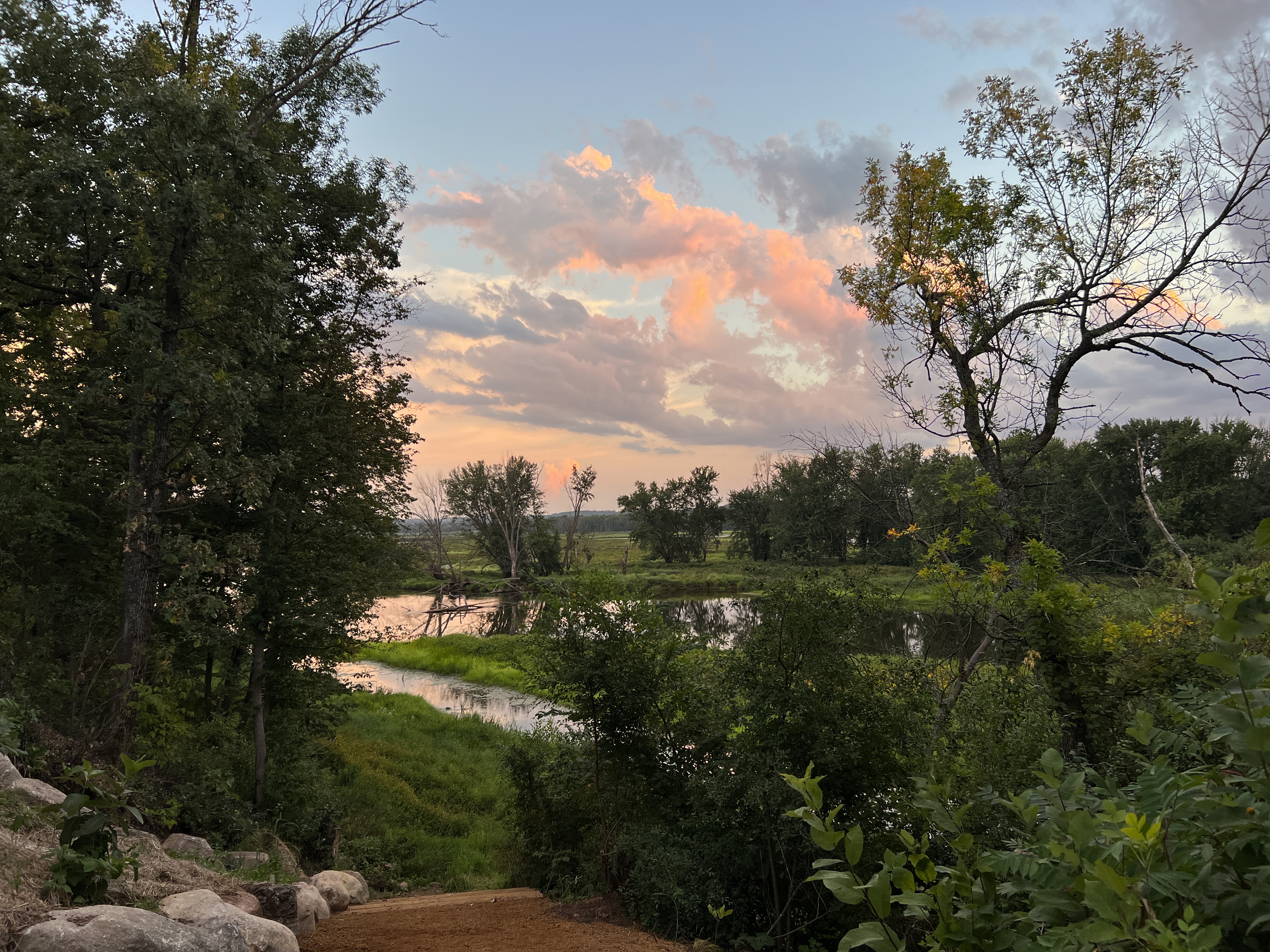 A peaceful riverbank view at dusk, showcasing vibrant sky colors and lush greenery.