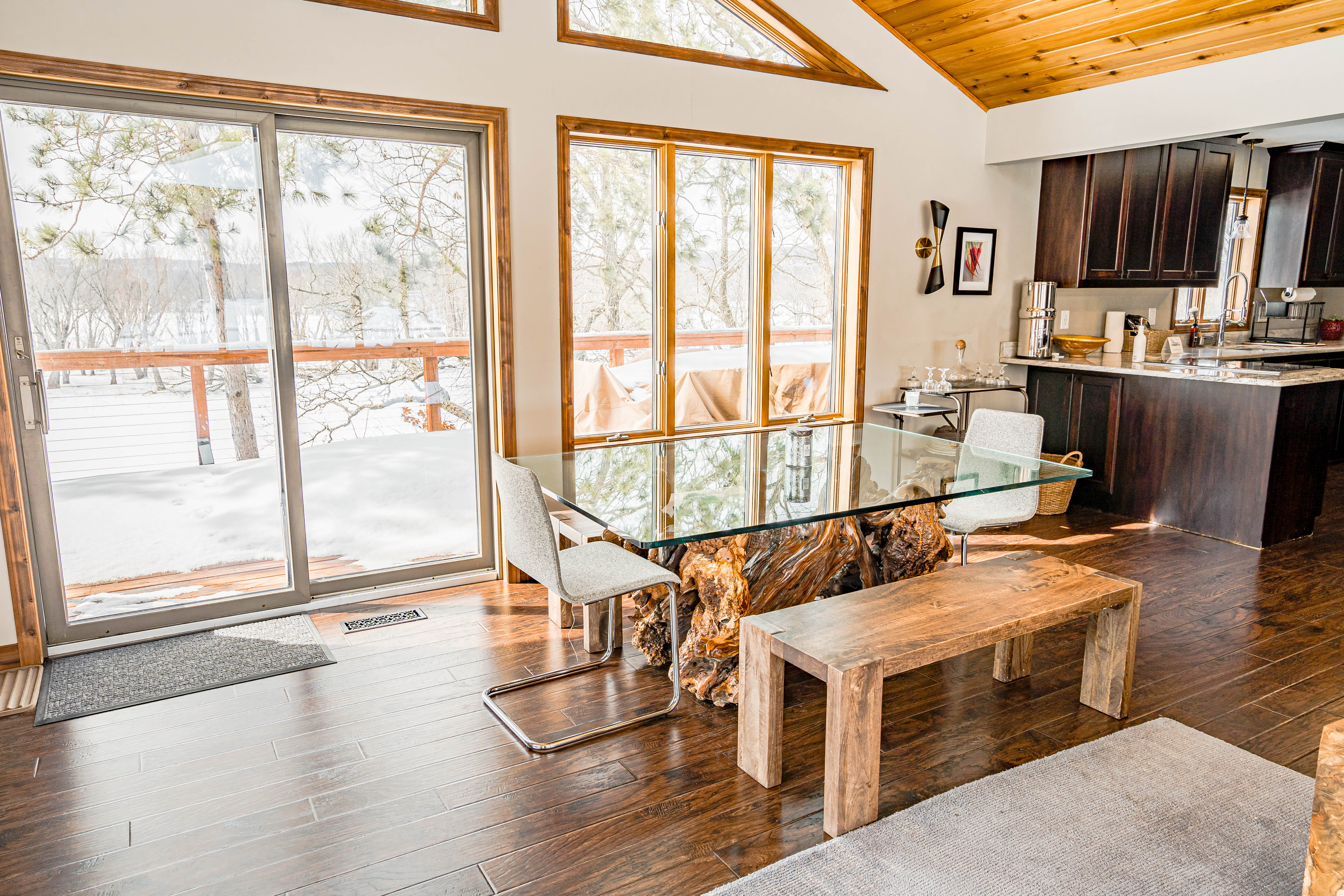 Modern dining area featuring a glass table with a wood base and winter views.