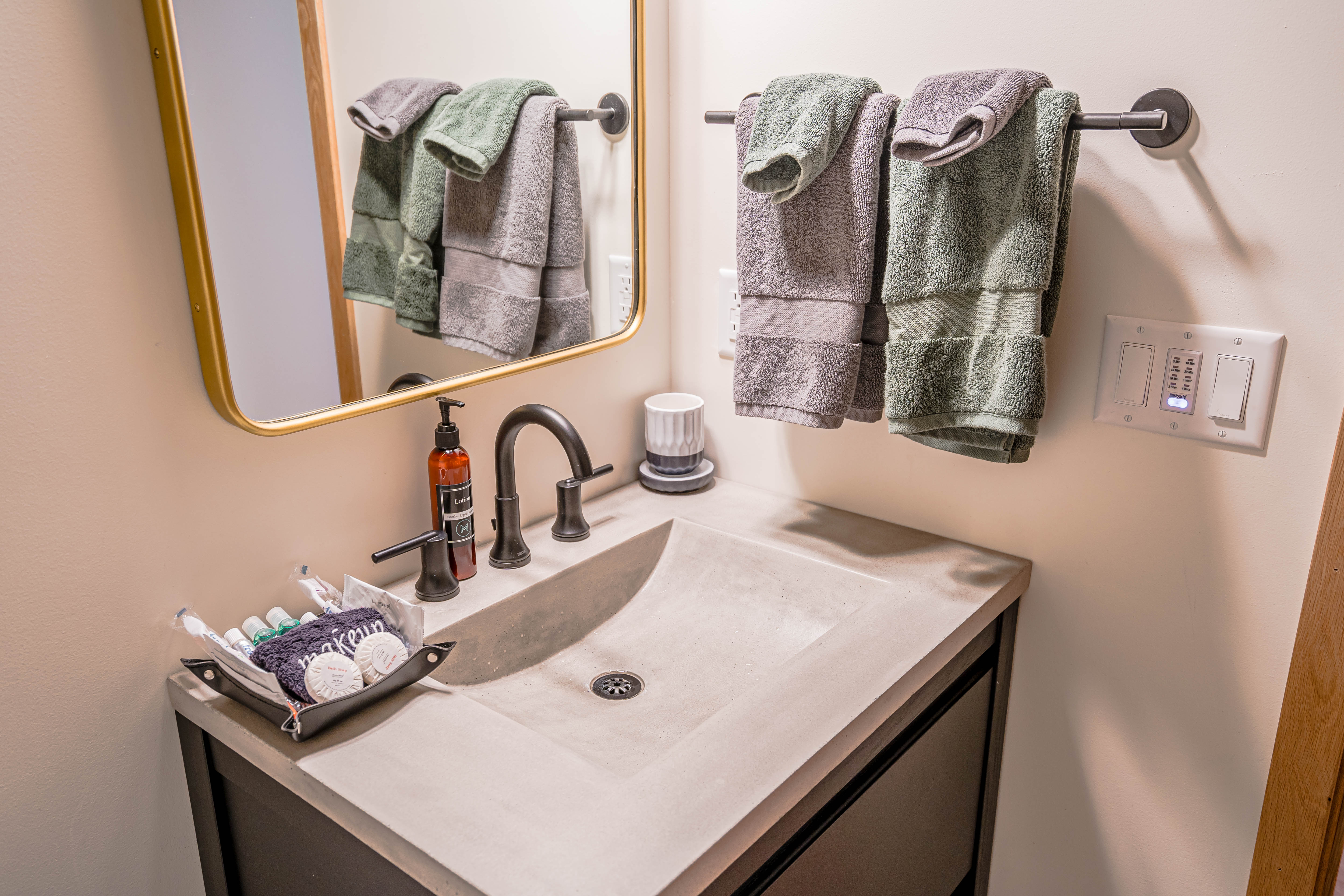 A modern bathroom sink area with concrete basin, neatly arranged toiletries, and stylish towels.