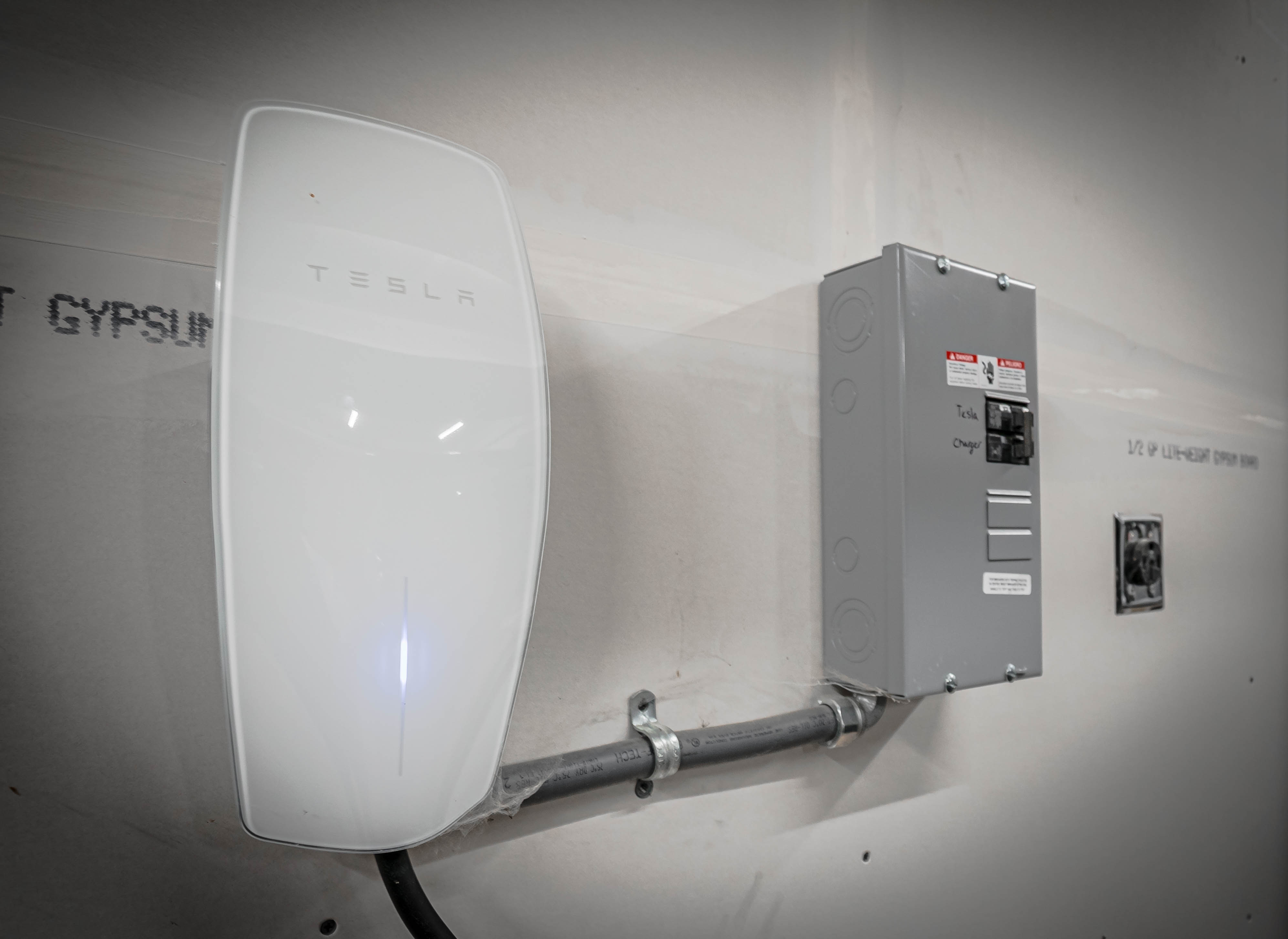 Tesla wall-mounted charger alongside an electrical sub-panel.