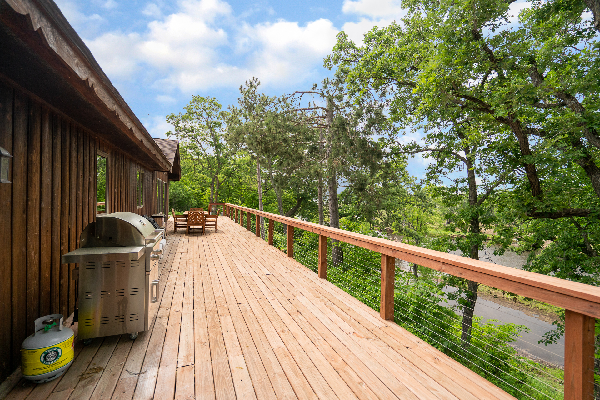 A wooden deck with a grill, overlooking a lush green landscape.