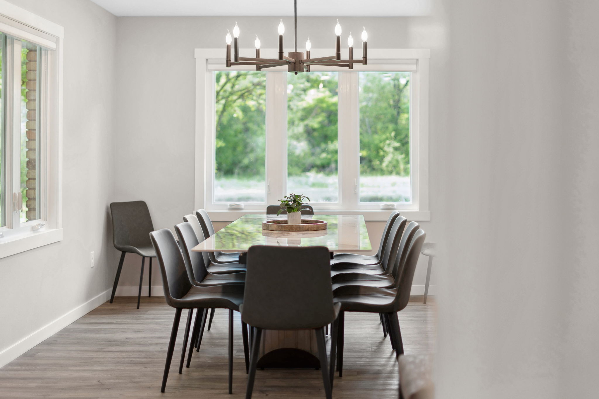 Modern dining room with a long table, dark chairs, and a chandelier.
