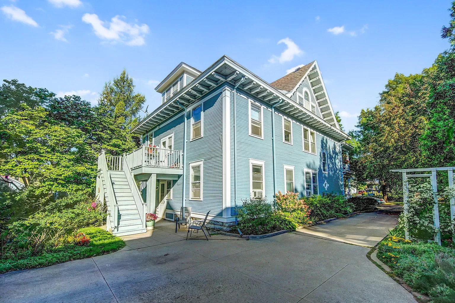 A picturesque blue house with a staircase and blooming garden, set against a sunny sky.