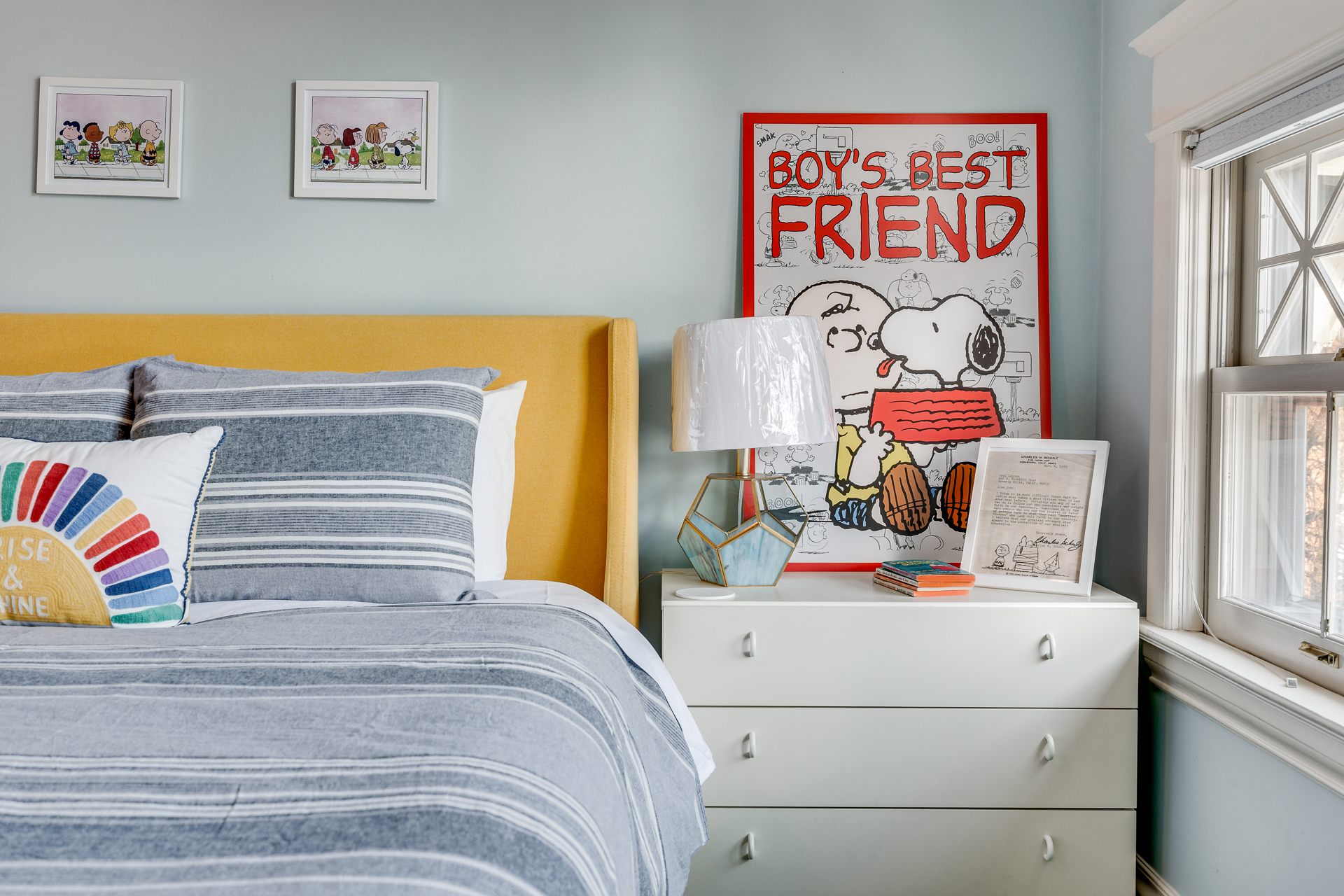 A cheerful bedroom featuring a yellow headboard, striped bedding, and playful artwork.
