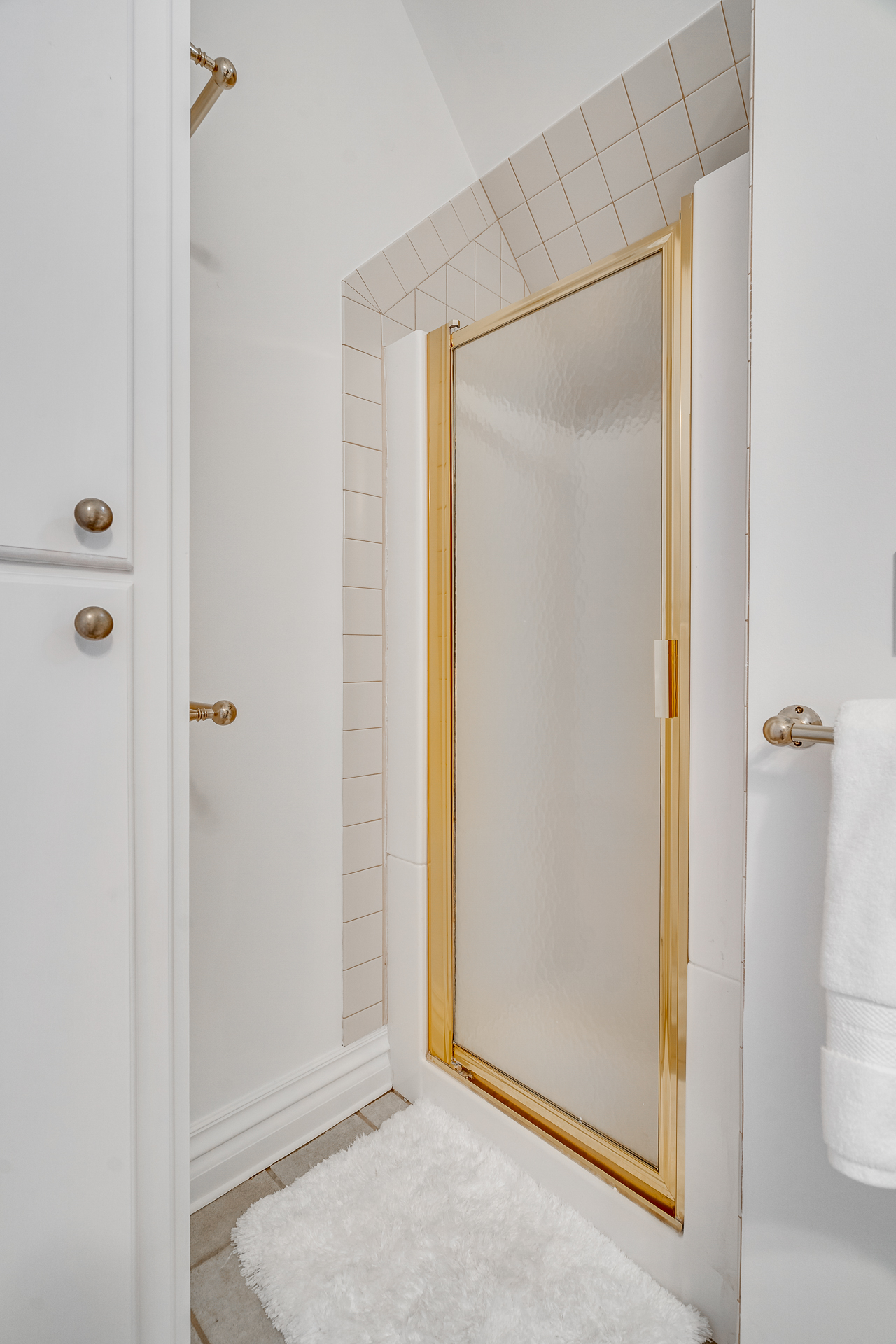 Elegant bathroom shower corner with a golden framed door and white tiles.