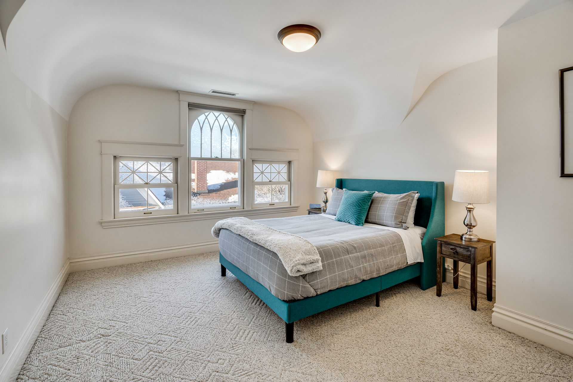 A cozy and inviting bedroom featuring a turquoise bed and unique curved ceiling.