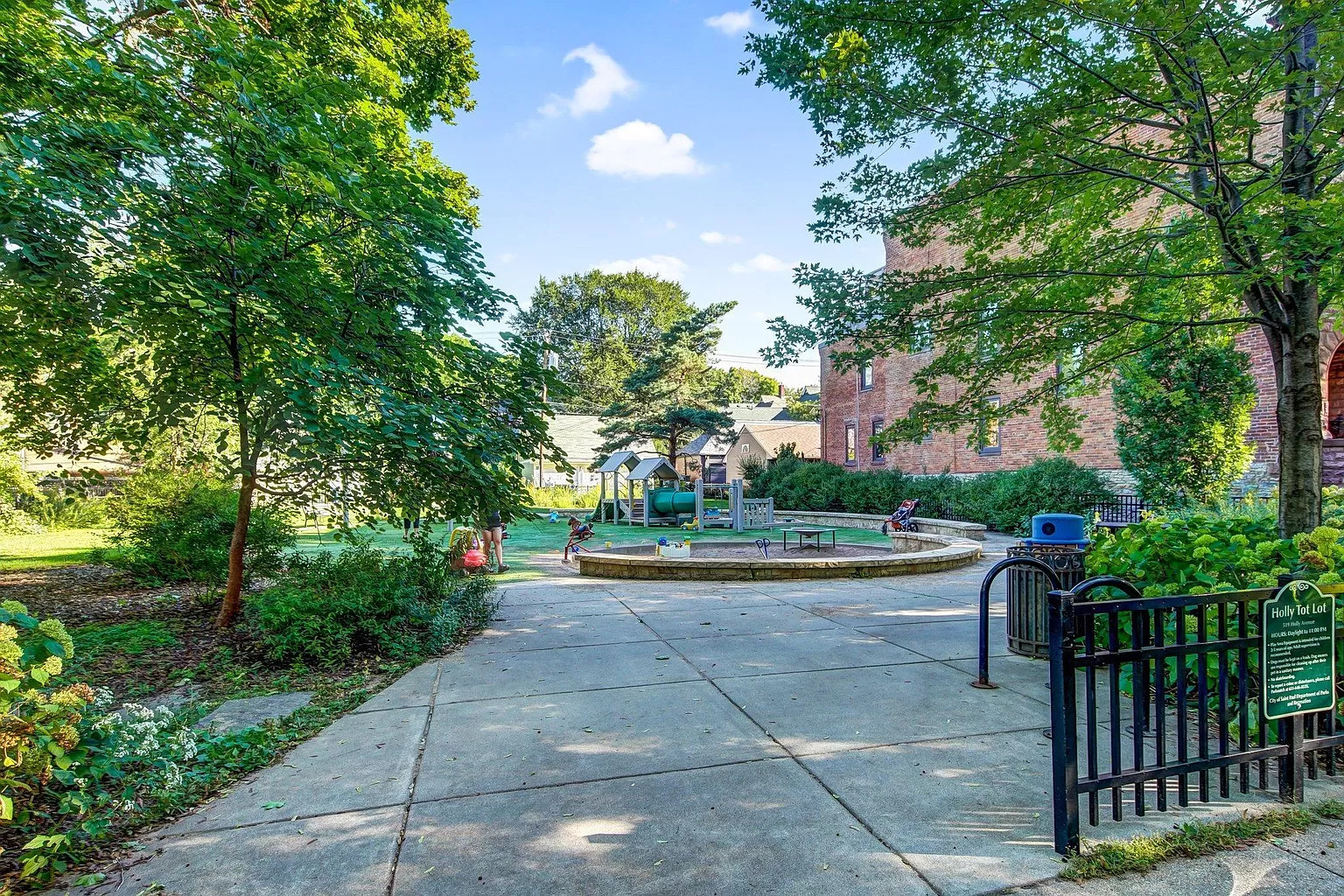A peaceful park with a play area surrounded by greenery and a brick building.