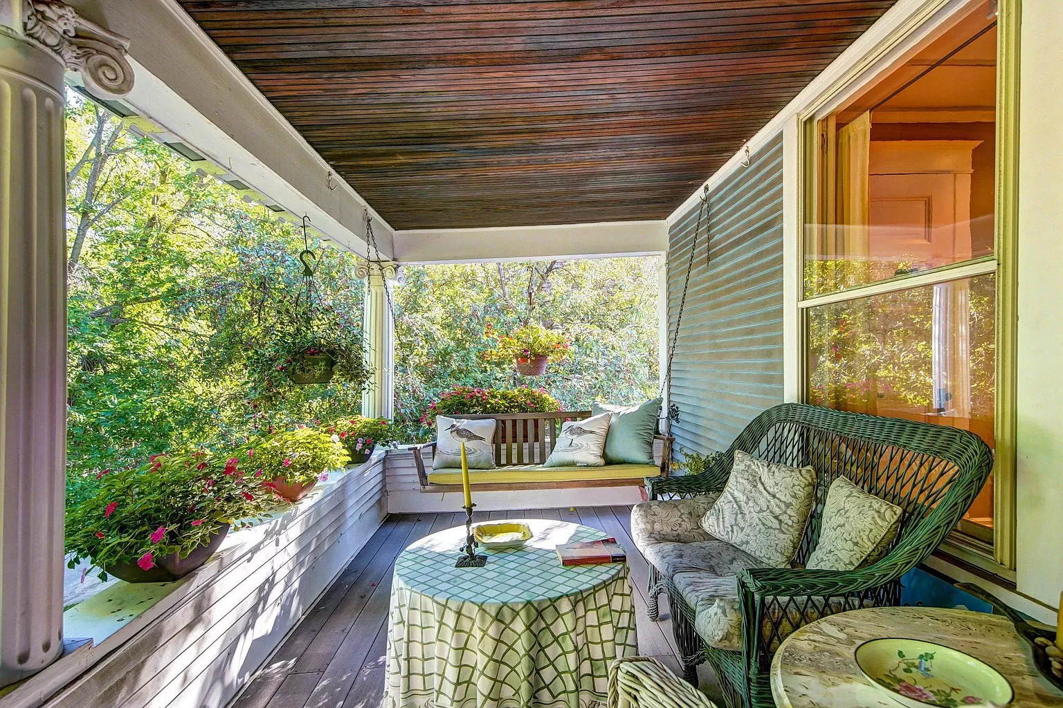 A cozy porch surrounded by greenery, featuring a swing and wicker seating.