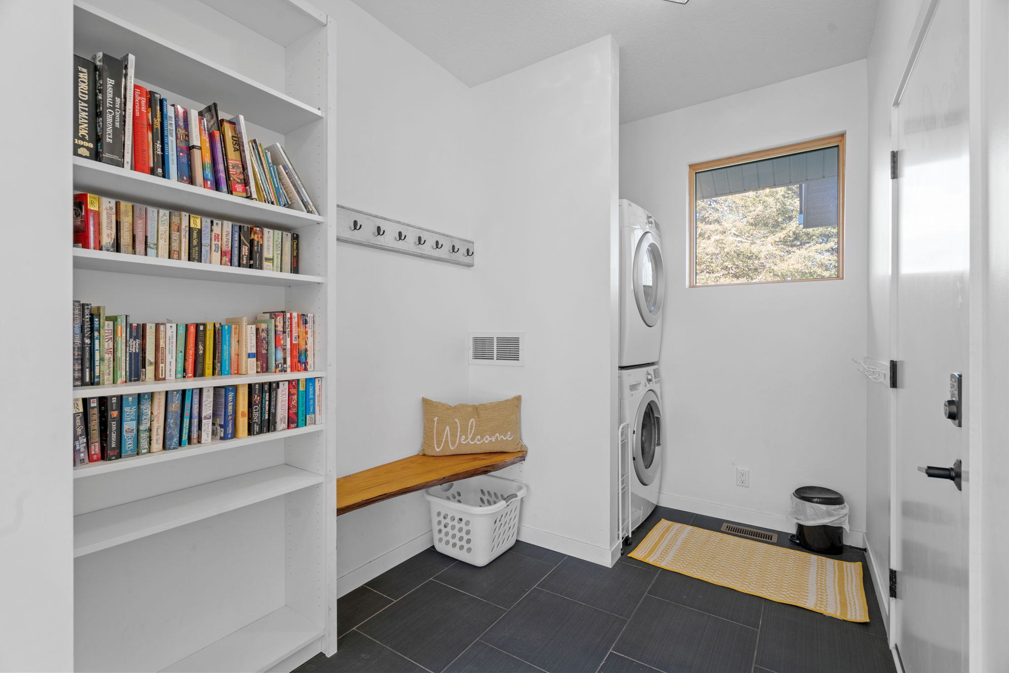 A bright and organized laundry room featuring a bookshelf, washer and dryer, and a welcoming bench.