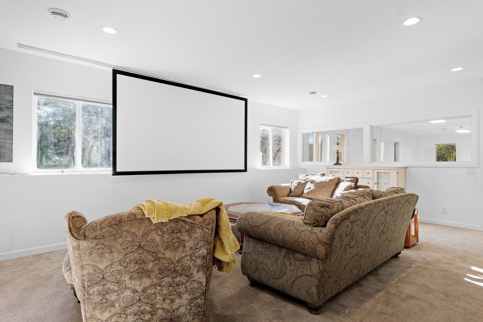 A cozy living room featuring a movie screen, plush furniture, and natural light.