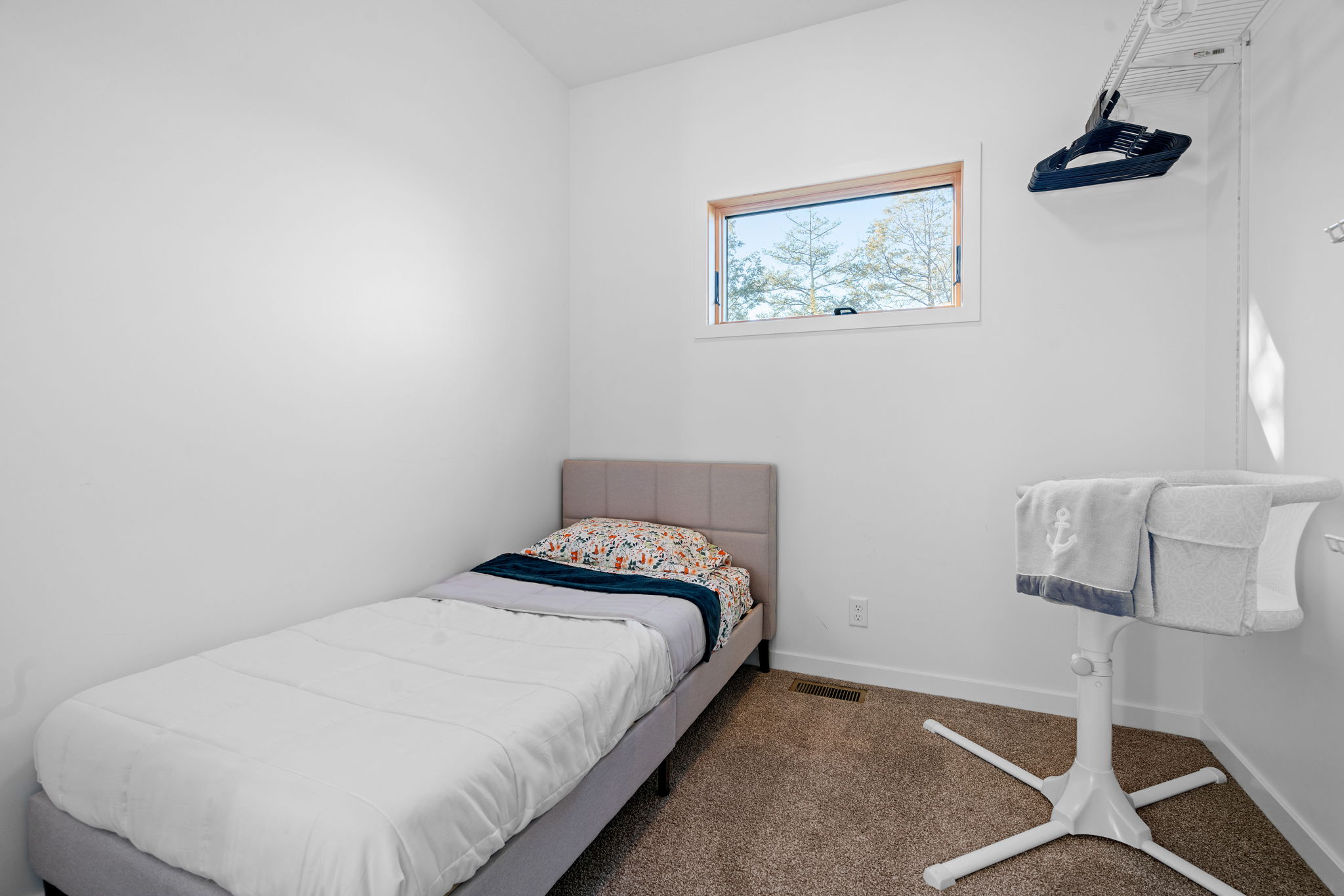 A cozy bedroom featuring a single bed and a modern baby bassinet.