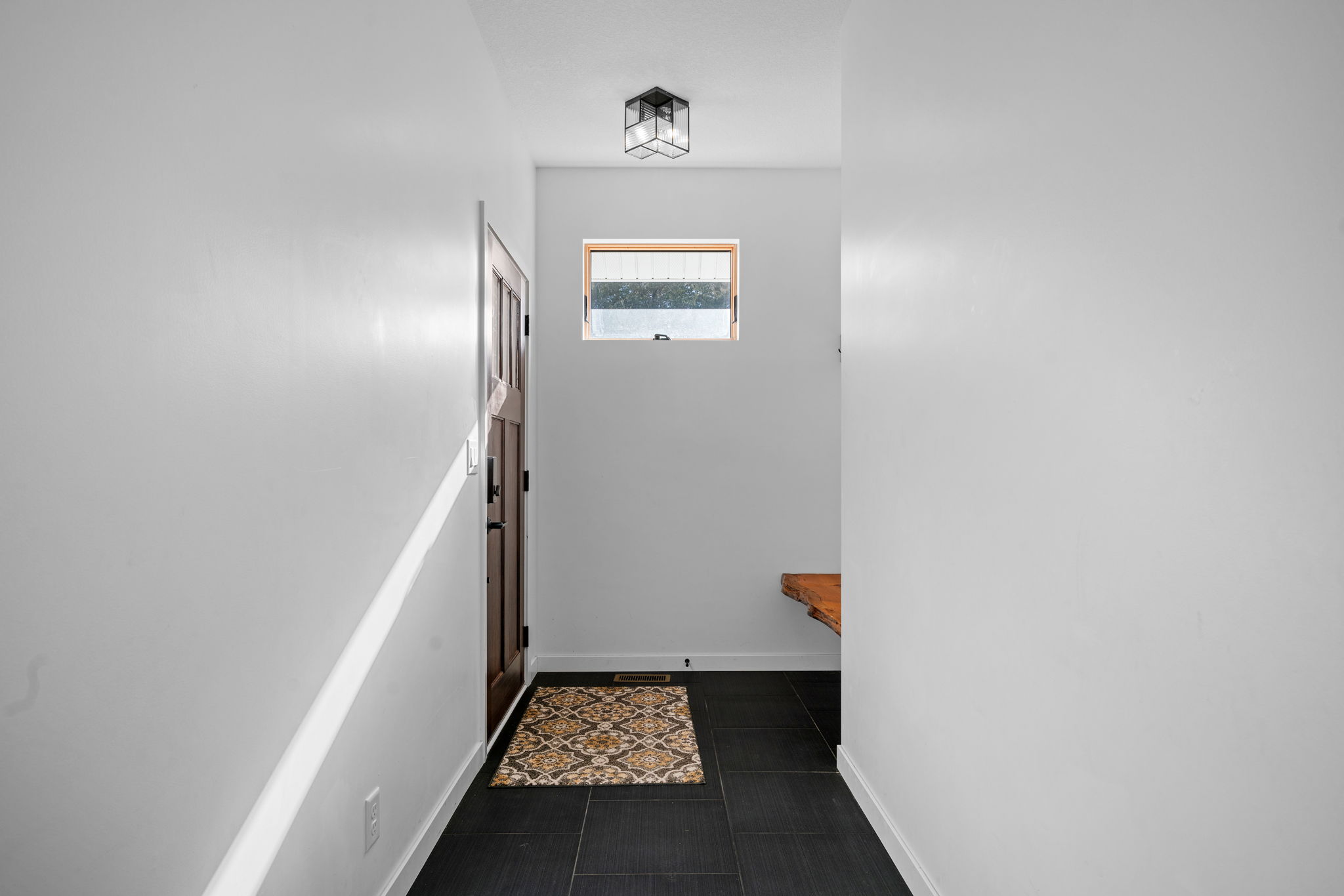 A bright, minimalist hallway with a wooden door and patterned doormat.