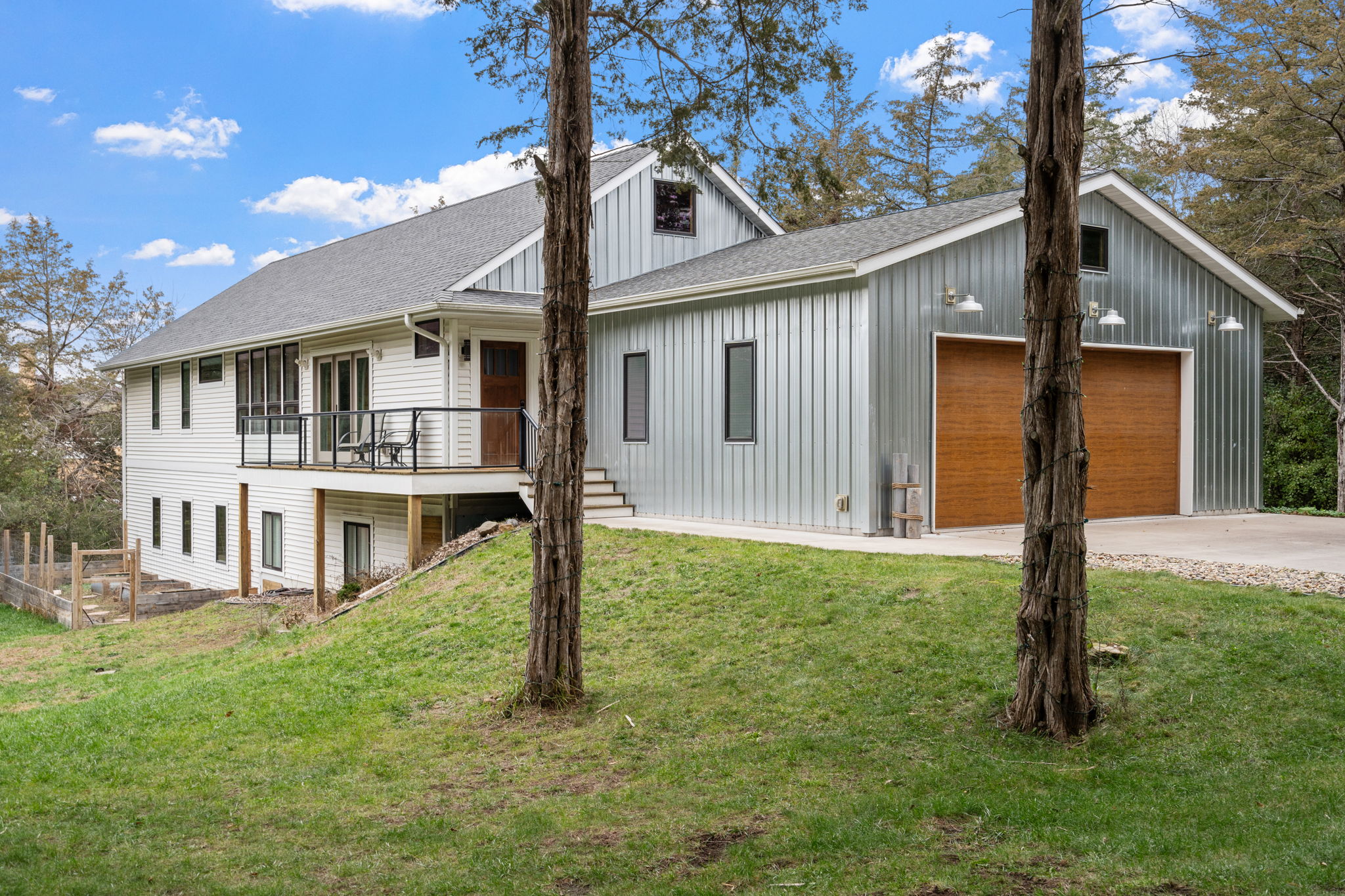 A modern two-story home with a combination of white and gray siding, set in a lush green landscape under a clear blue sky.