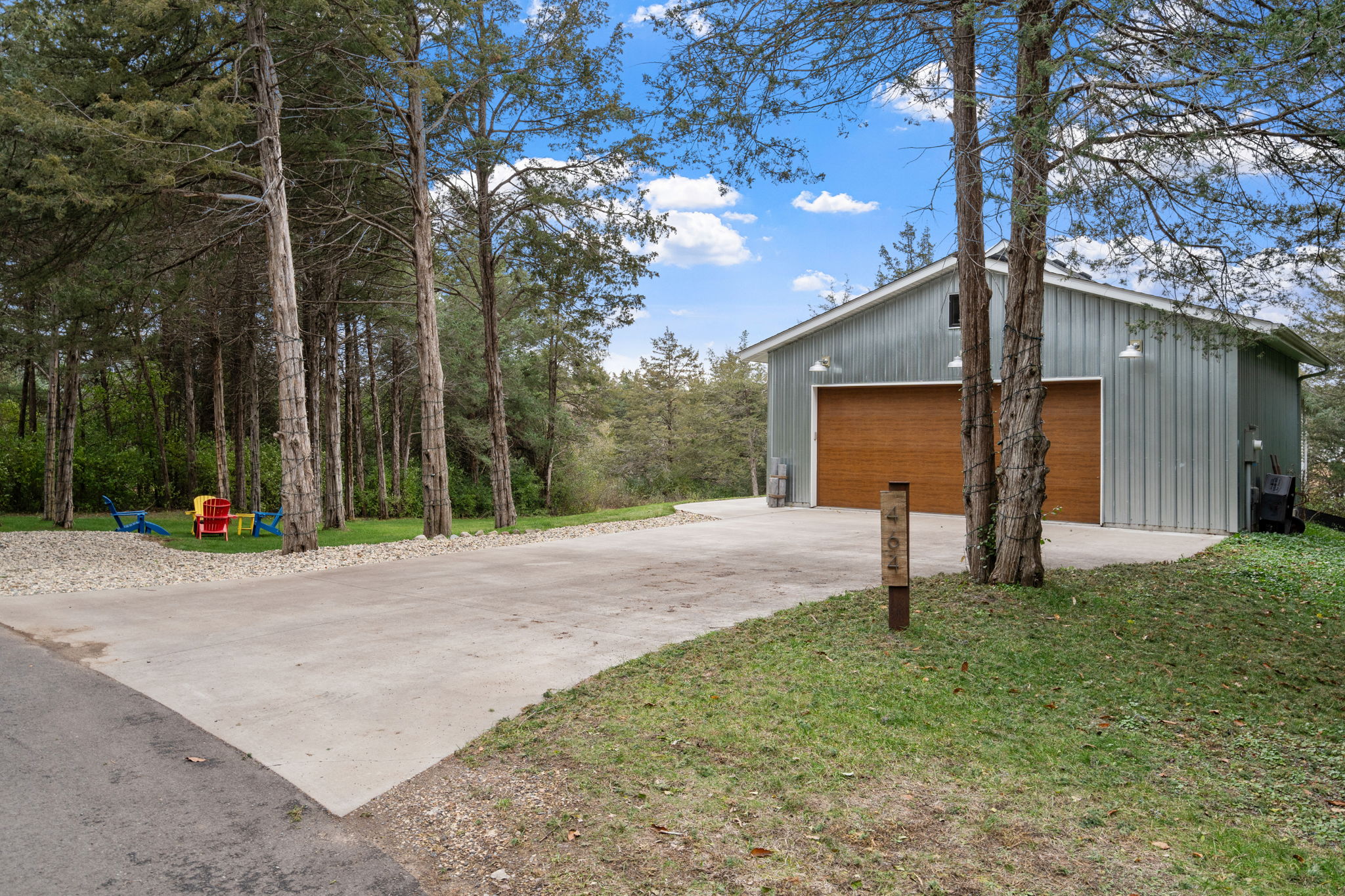 A tranquil outdoor scene featuring a garage and colorful Adirondack chairs amidst tall trees.