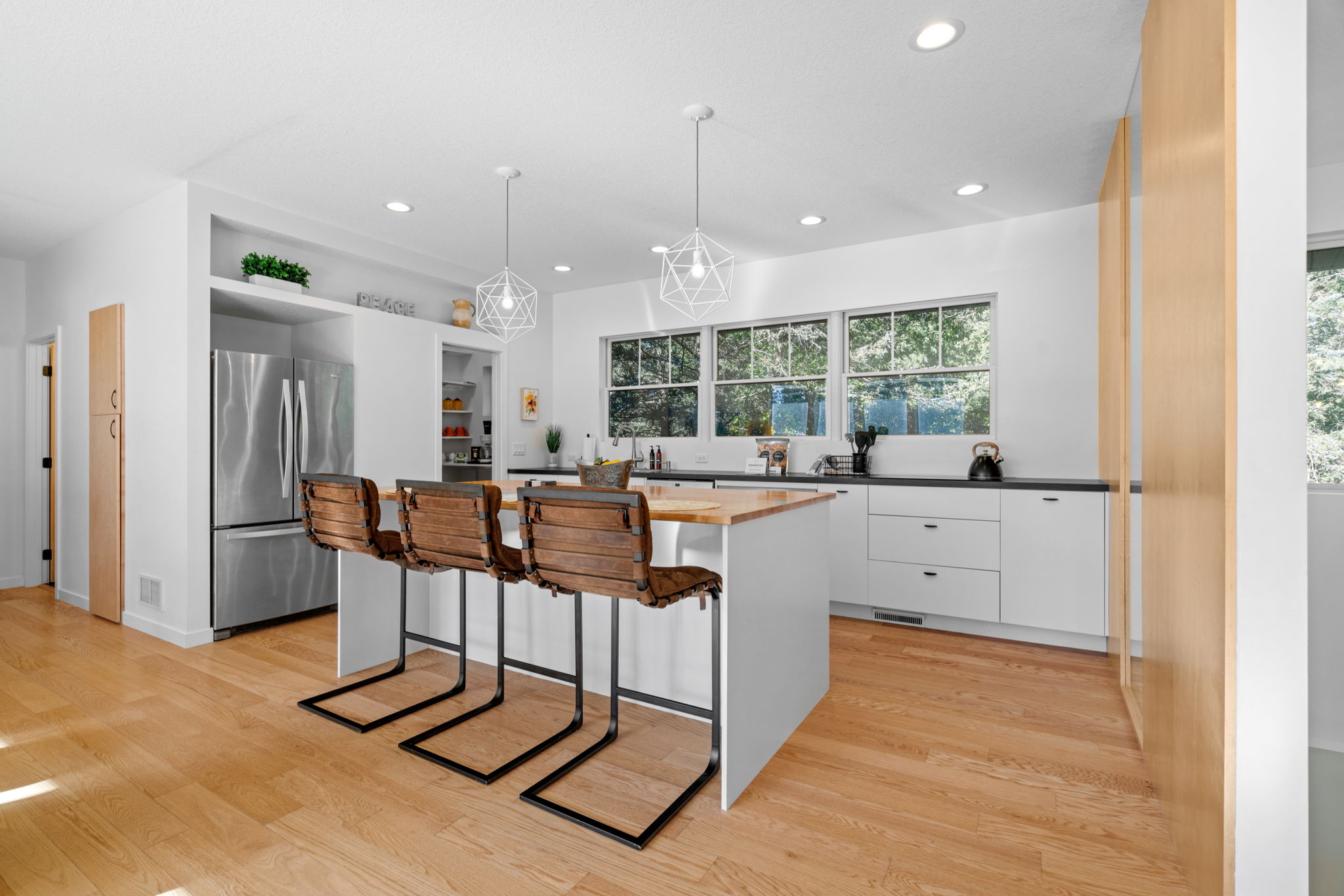 A modern minimalist kitchen with a wooden island and stylish bar stools.