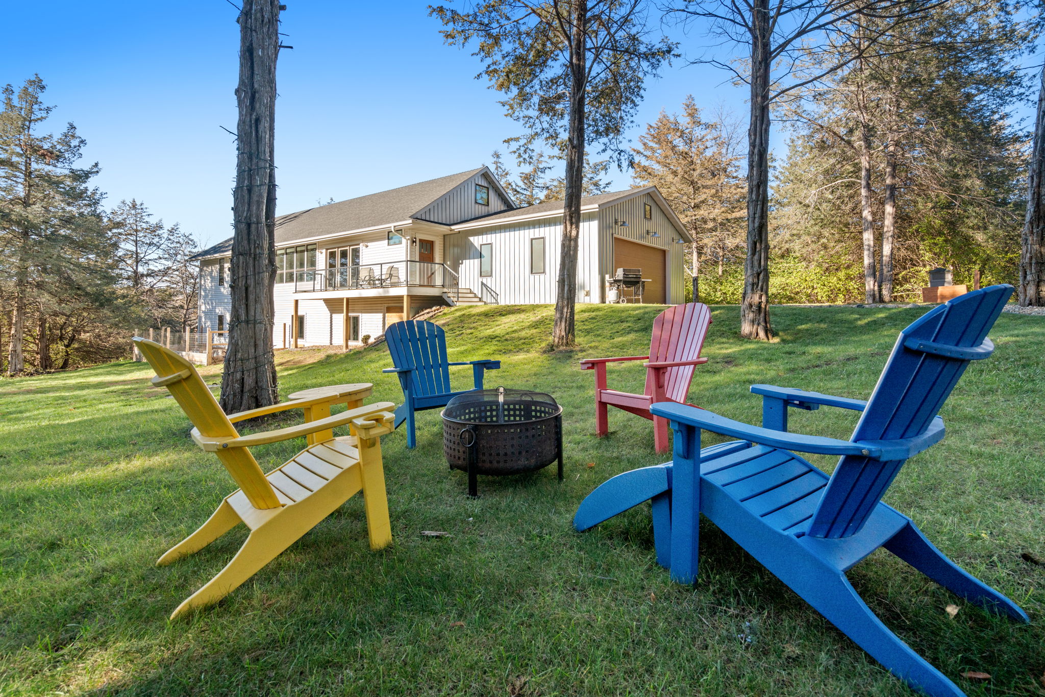 Colorful Adirondack chairs around a fire pit near a modern home.
