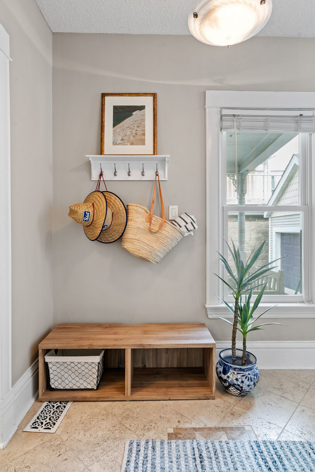 A welcoming entryway featuring a wooden bench, stylish hats, and a beach-themed photo.