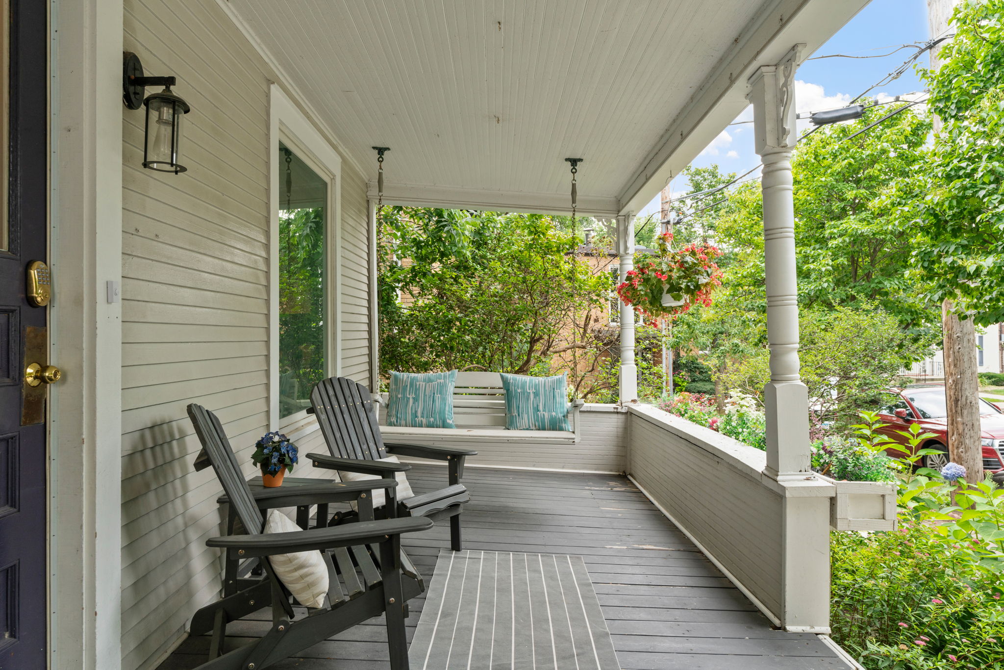 A cozy porch with Adirondack chairs, a swing, and lush greenery.