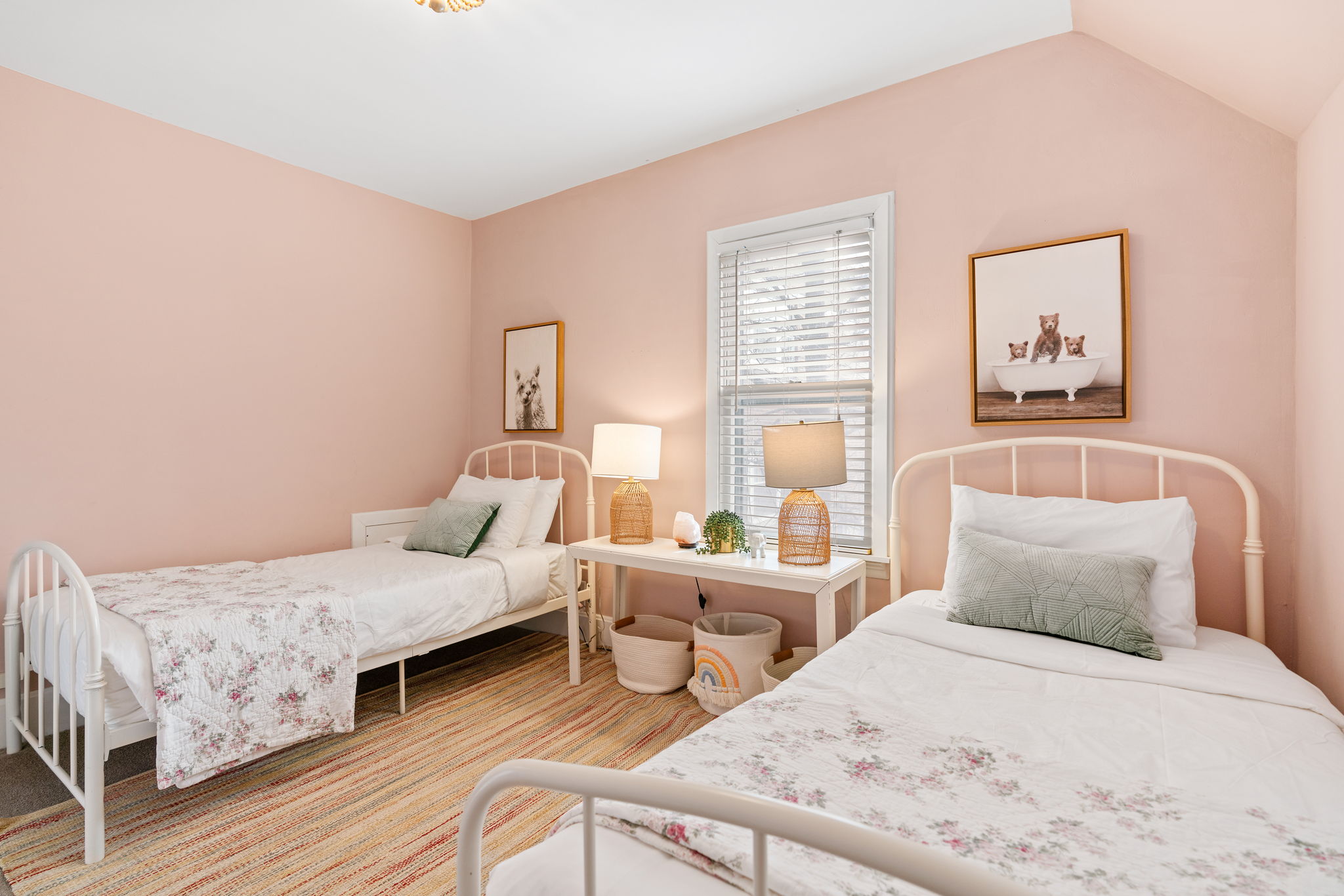 A cozy children's bedroom with twin beds and soft pink walls.
