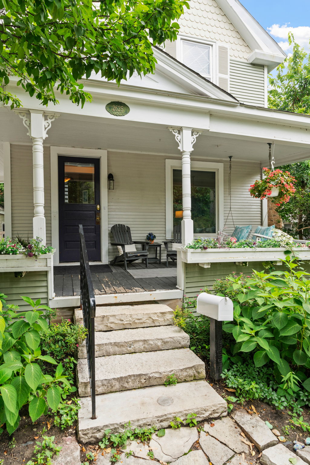 Charming front porch of a two-story home with stone steps and flower baskets.
