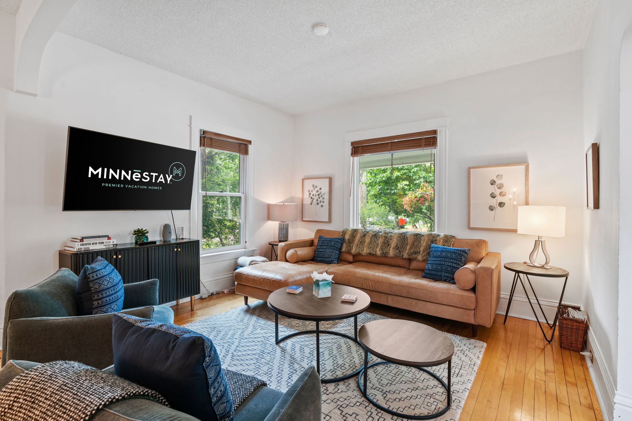 Modern living room with a light brown leather sofa, plush armchairs, and natural light from windows.