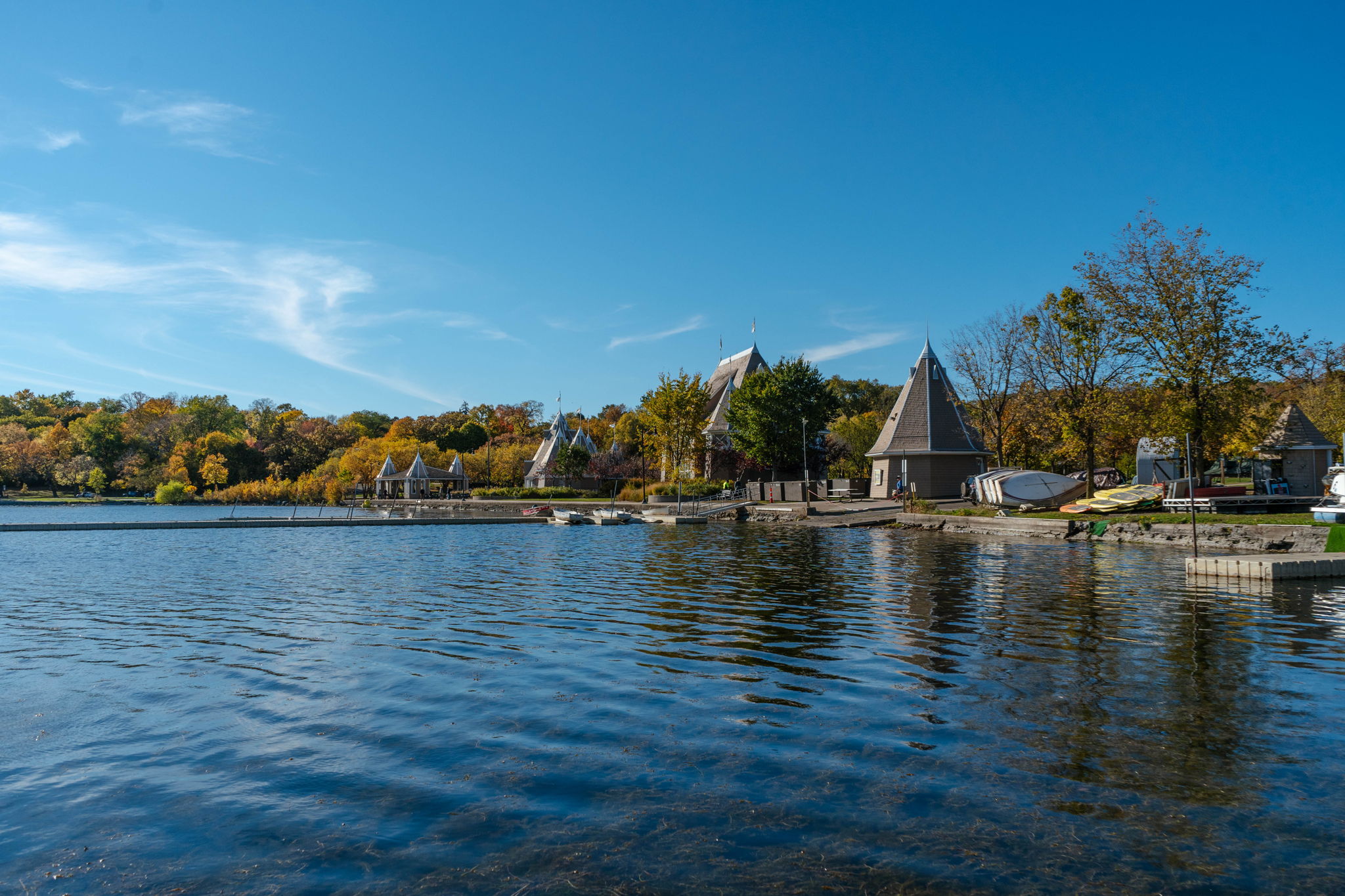 Serene lakeside view with autumn foliage and conical-roofed structures.