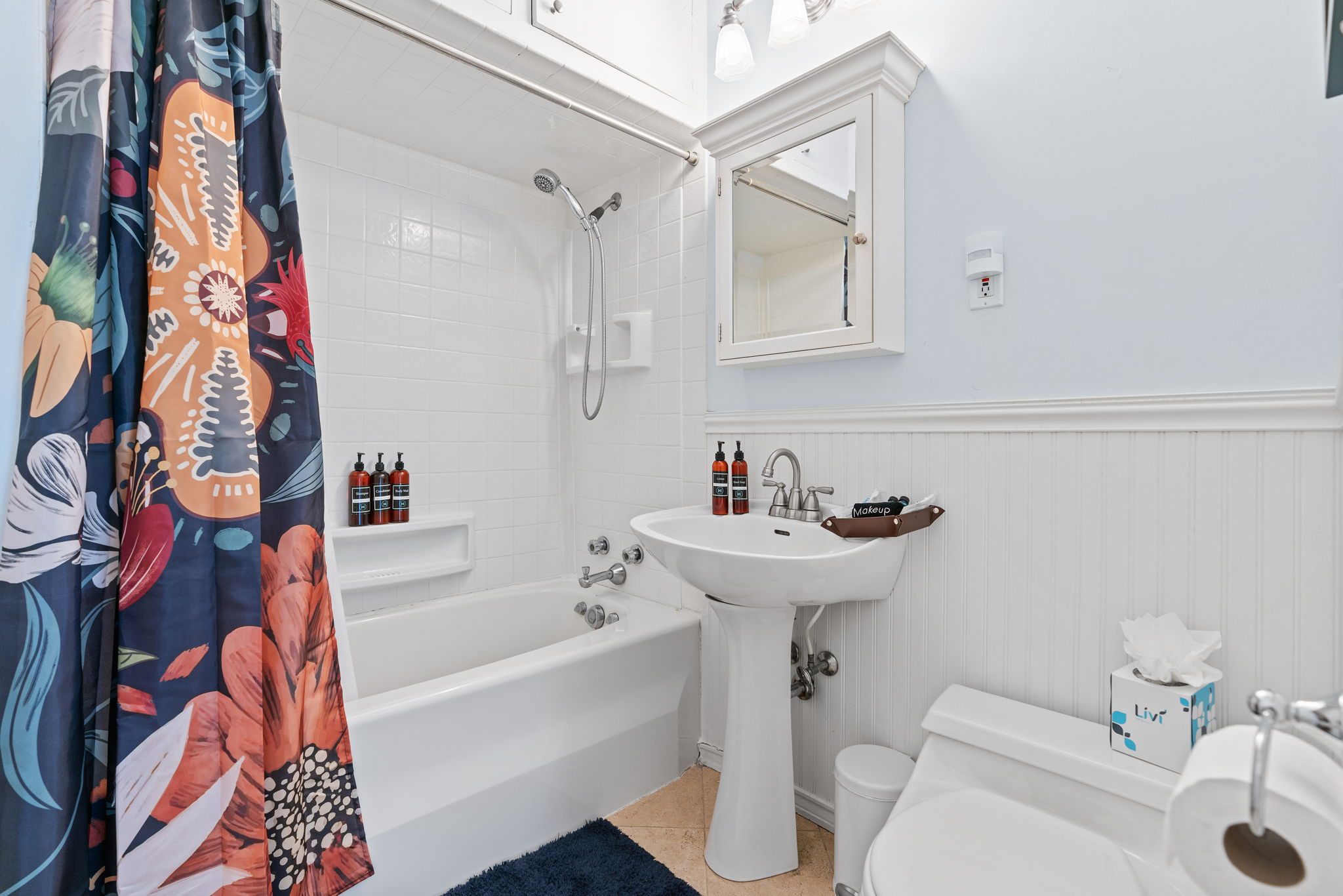 A colorful and modern bathroom featuring a floral shower curtain and a sleek pedestal sink.