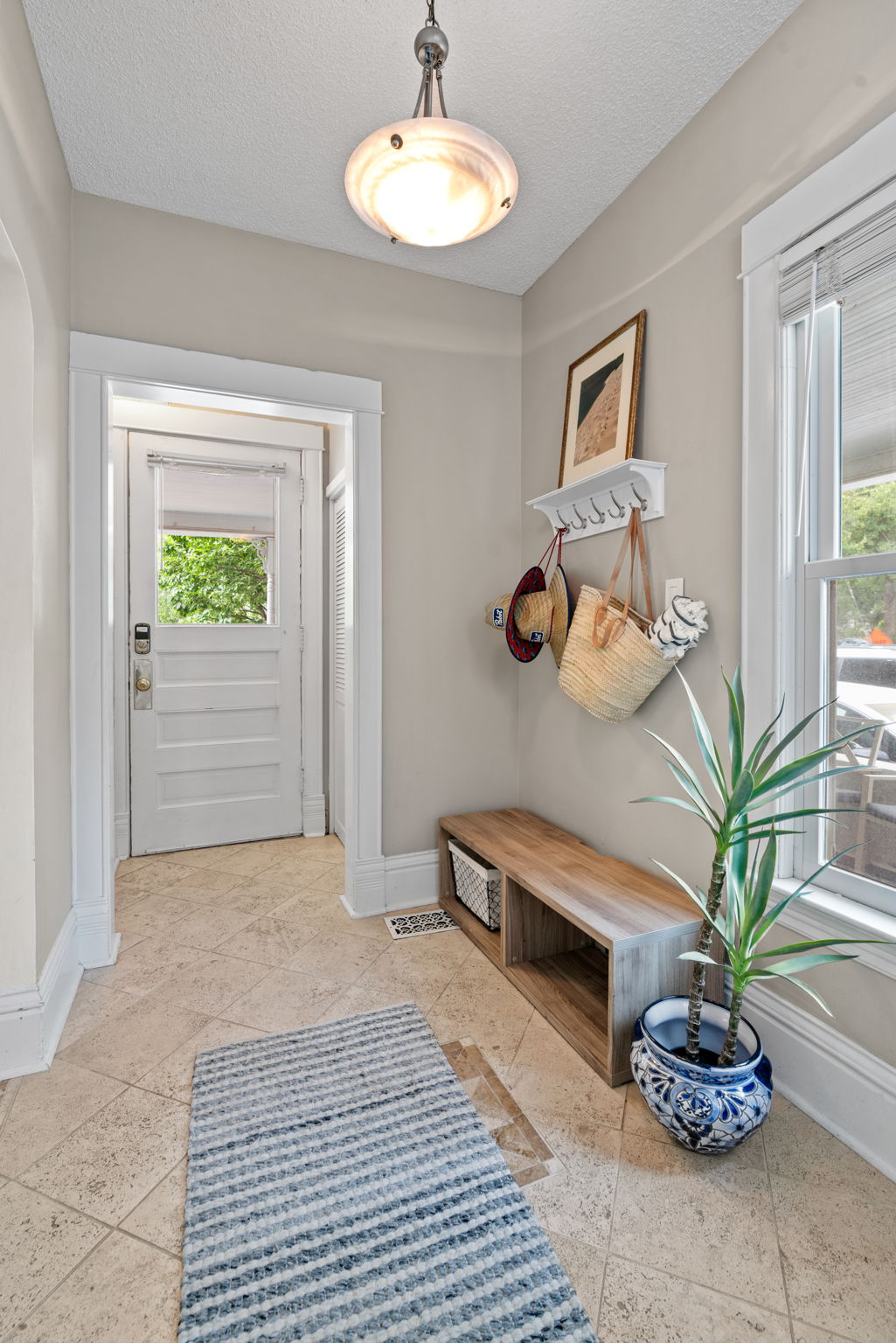 A bright and inviting entryway featuring a pendant light, wooden bench, and stylish decor.
