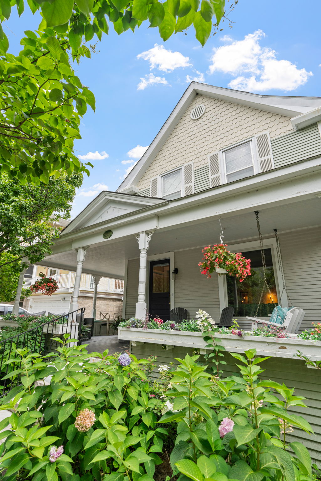 A charming house with a beautiful porch surrounded by flowers and vibrant greenery.