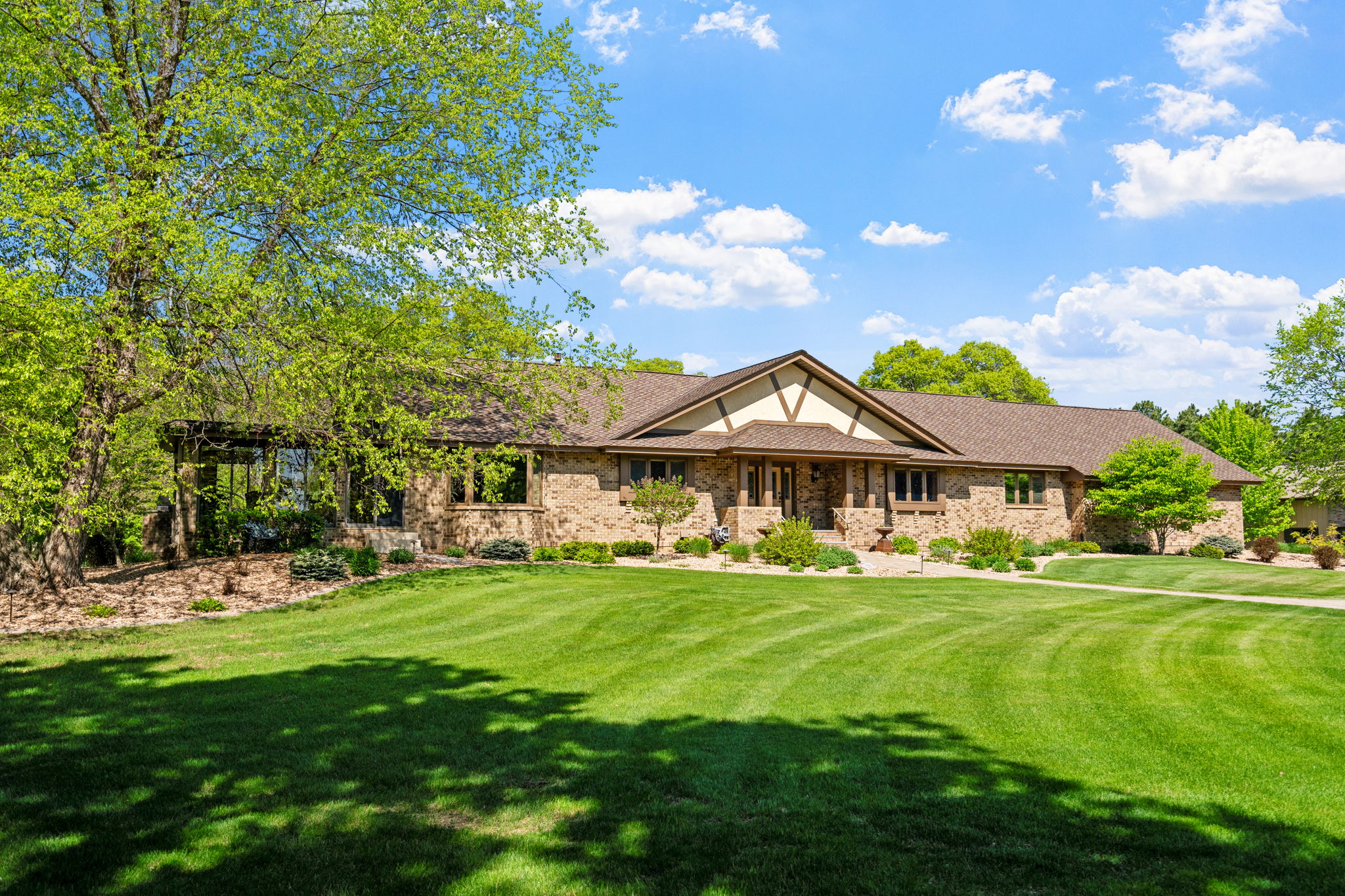 A beautifully landscaped brick home with a large lawn and clear blue sky.