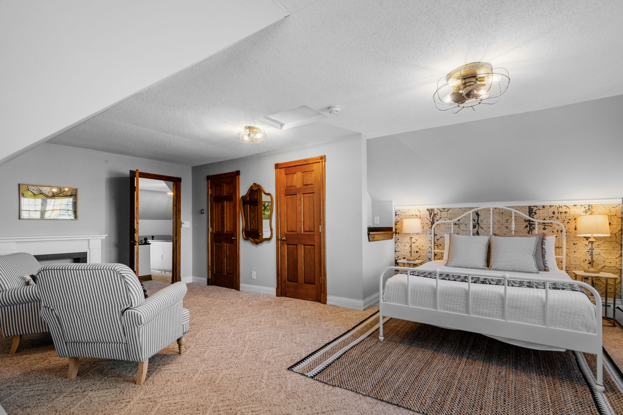 A cozy and elegantly designed bedroom featuring a double bed, striped armchairs, and warm lighting.