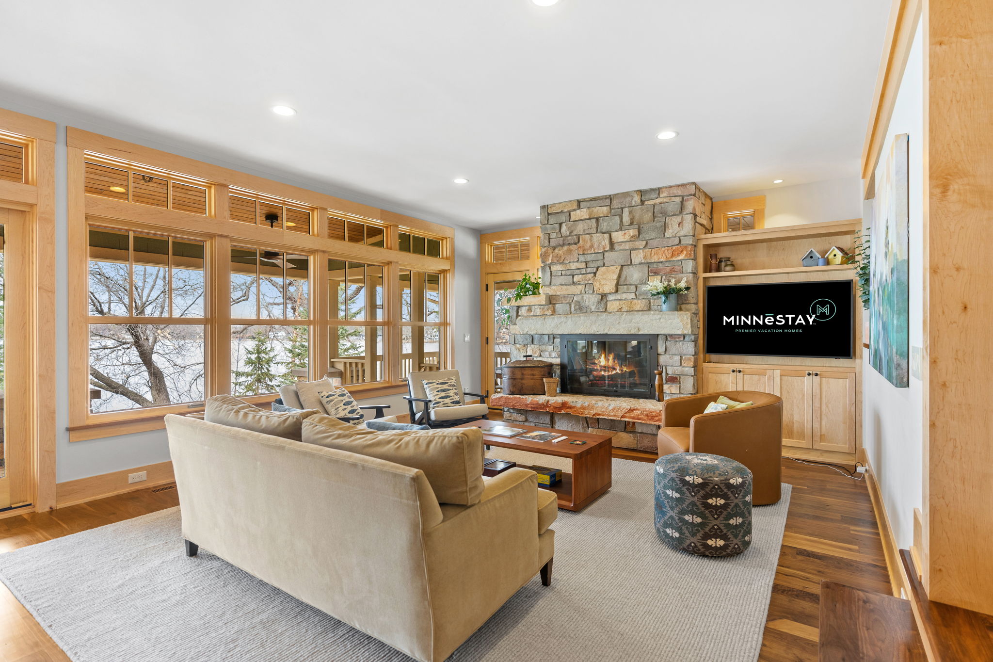 Bright living room featuring a stone fireplace, large windows, and comfortable seating.