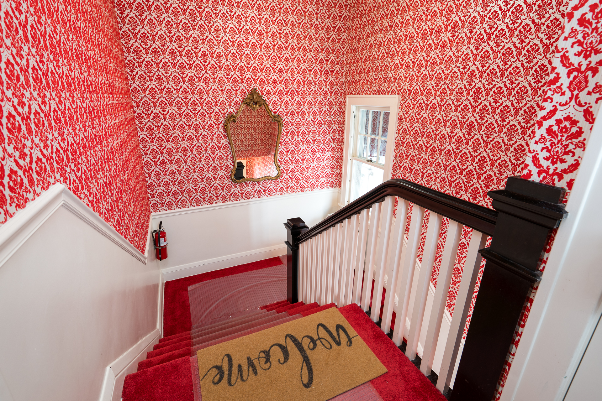 A colorful staircase with vibrant red wallpaper and a welcome mat.