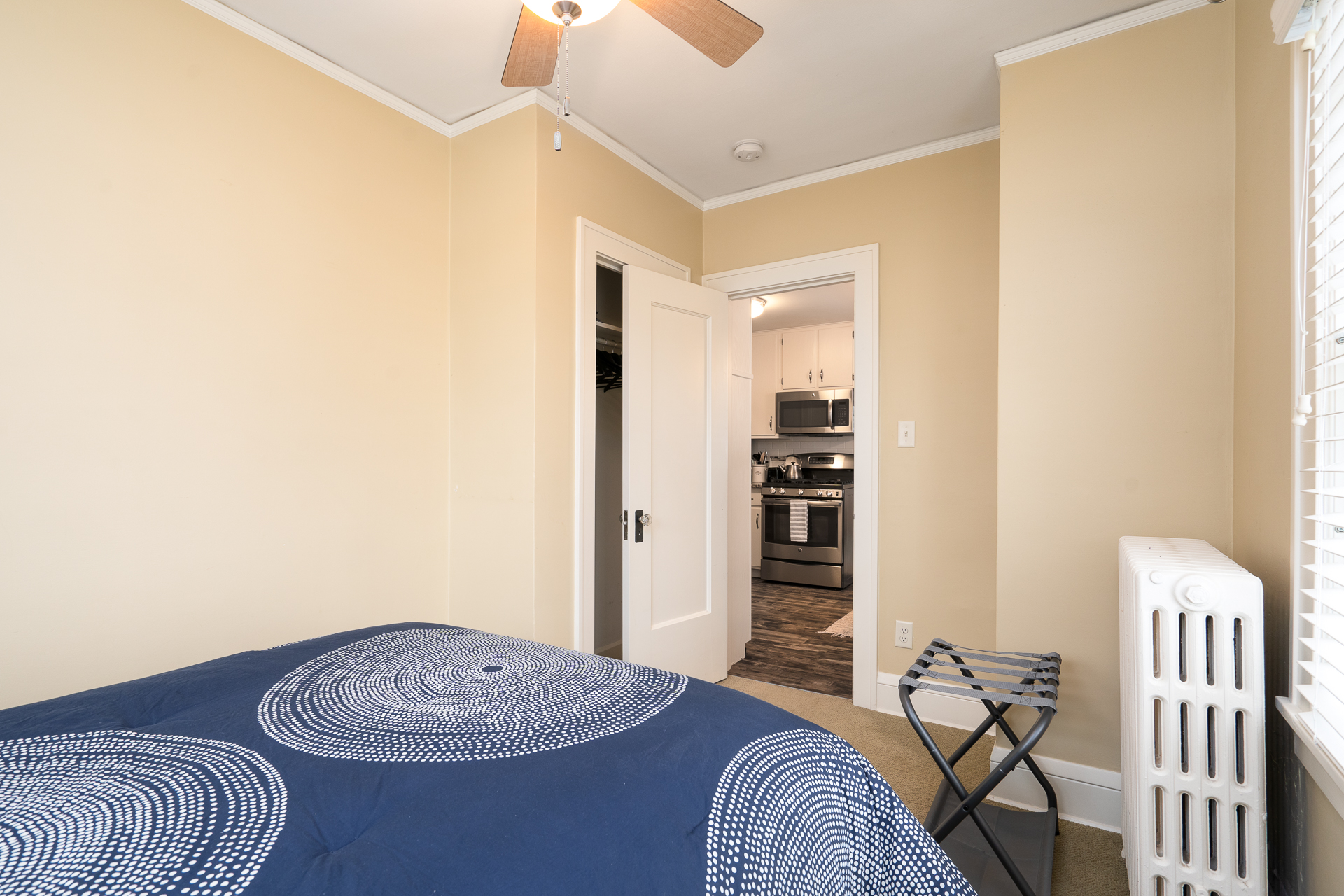 A cozy bedroom leading to a modern kitchen, featuring a stylish bed and vintage radiator.