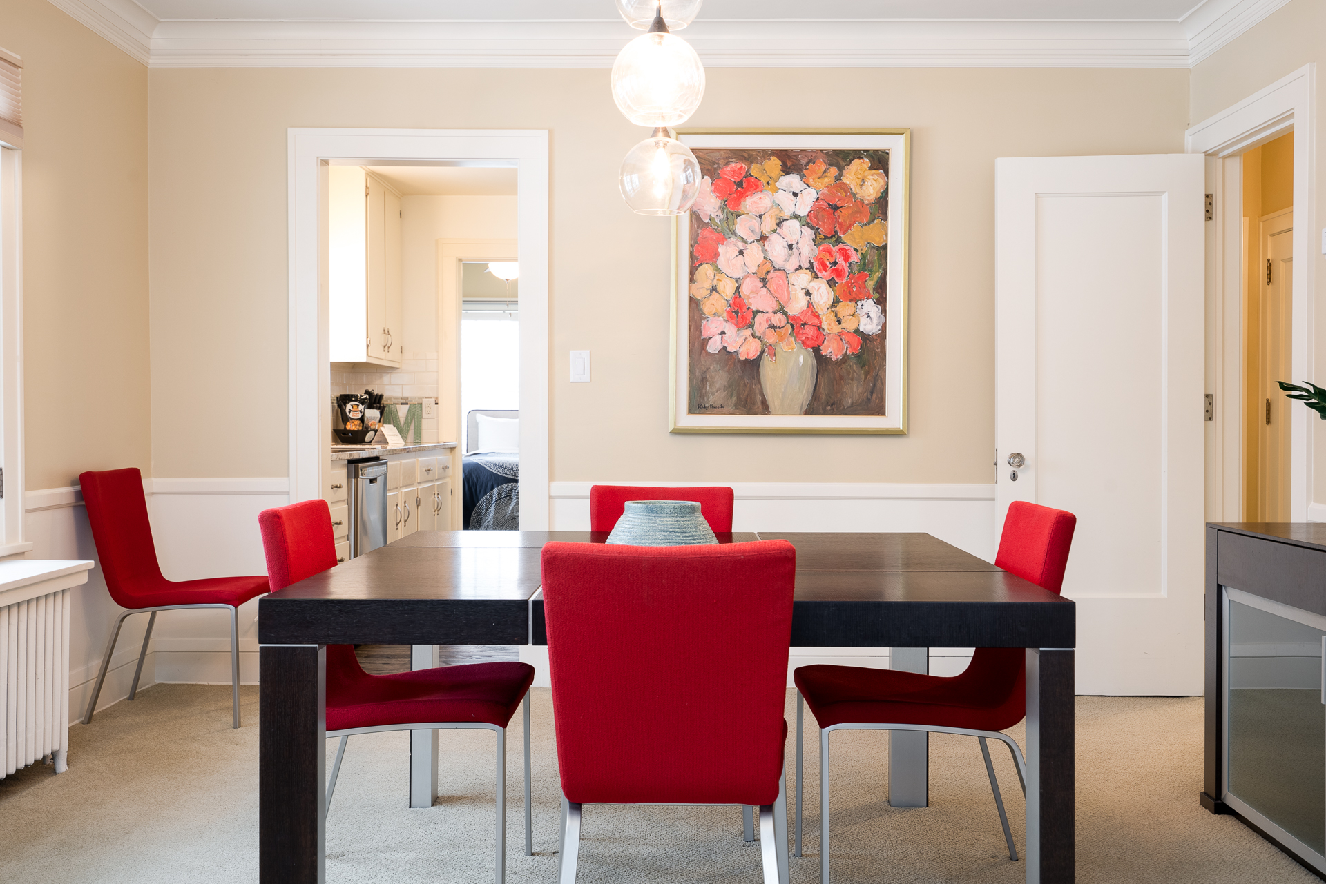 Bright and inviting dining area with modern red chairs and a vibrant floral painting.