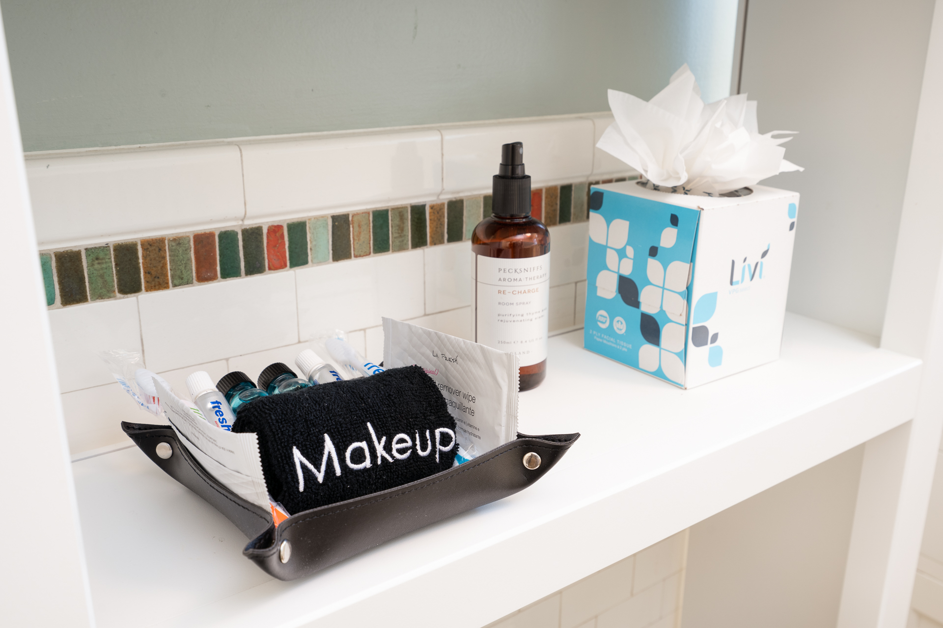 A stylish bathroom shelf organized with personal care items, including a makeup towel, small bottles, and a room spray.