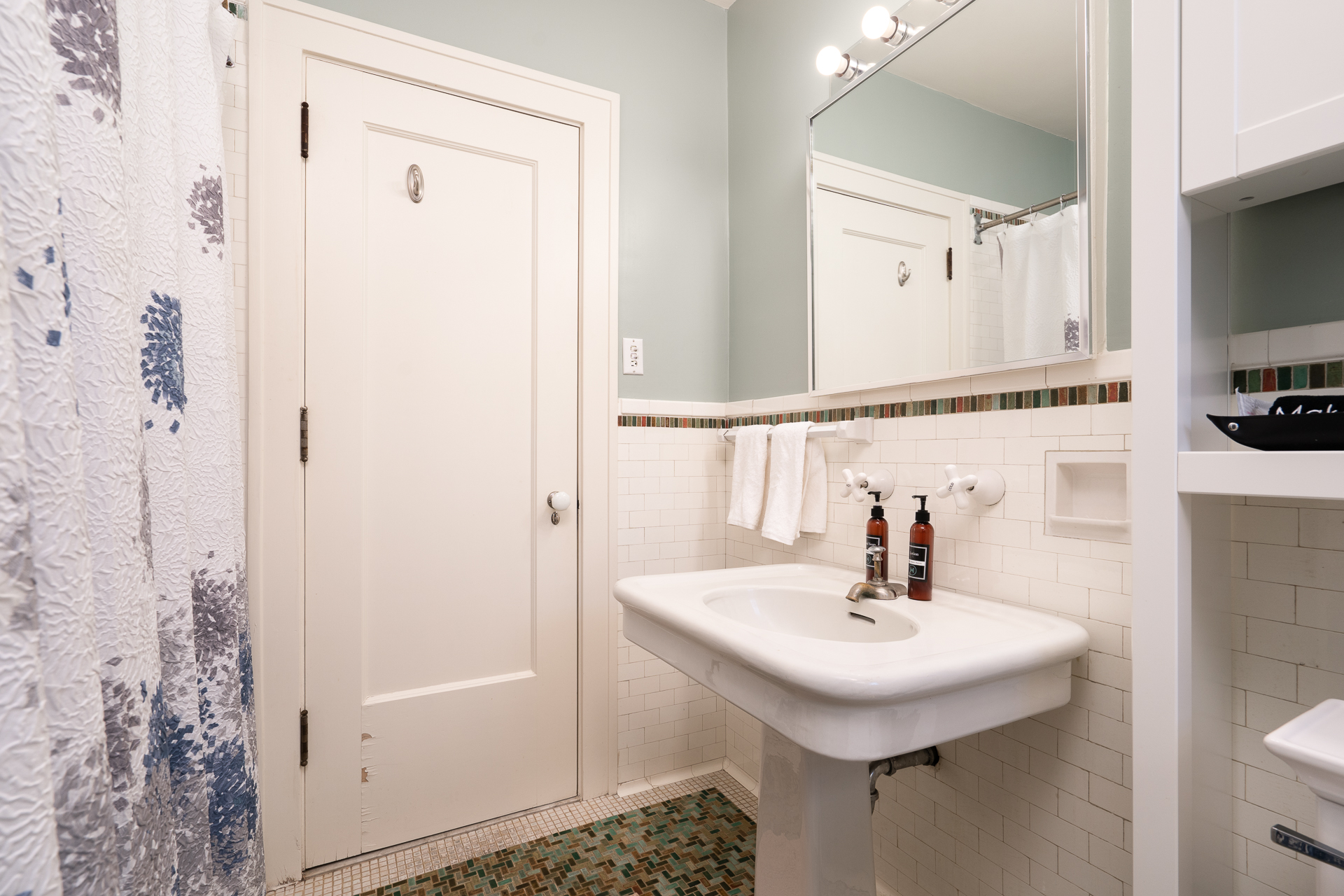 A modern bathroom featuring a stylish sink, patterned shower curtain, and decorative tile accents.