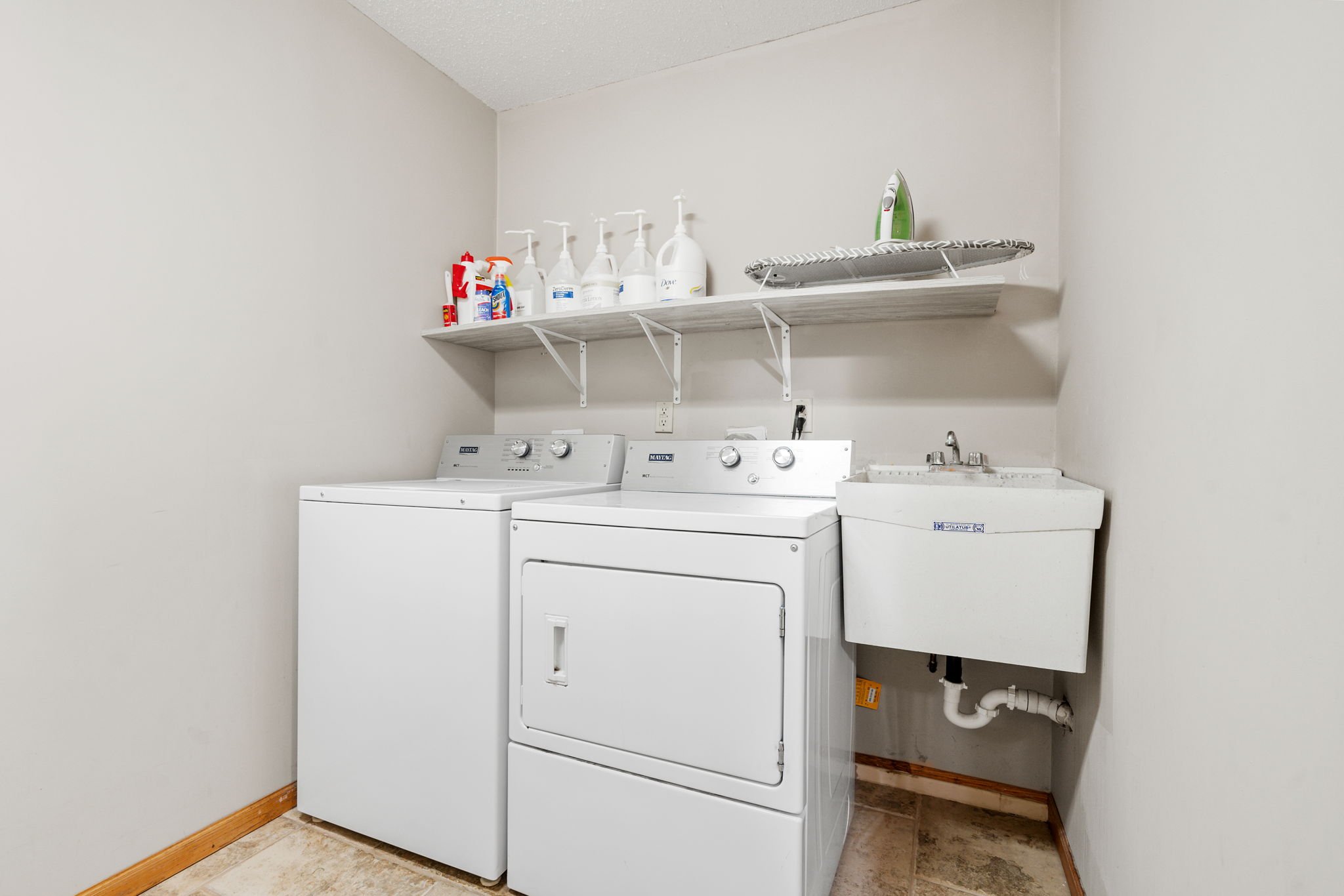 A tidy laundry room featuring a washer and dryer with cleaning supplies and a utility sink.