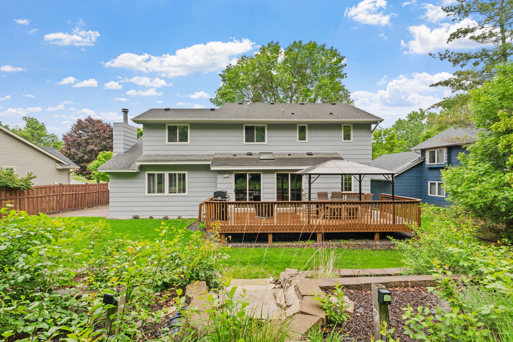 A beautiful backyard view showcasing a two-story gray house with a welcoming deck and lush greenery.