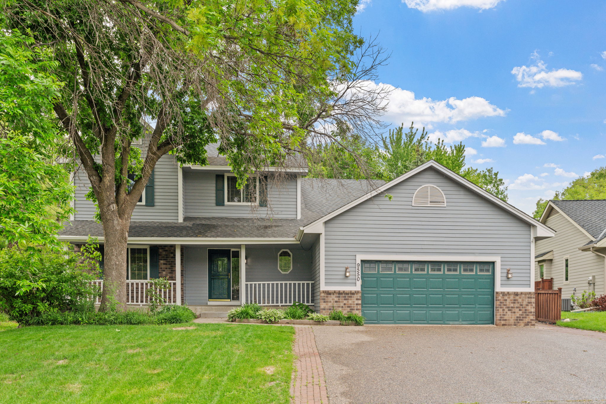 A two-story house with gray siding, teal garage door, and a green lawn.