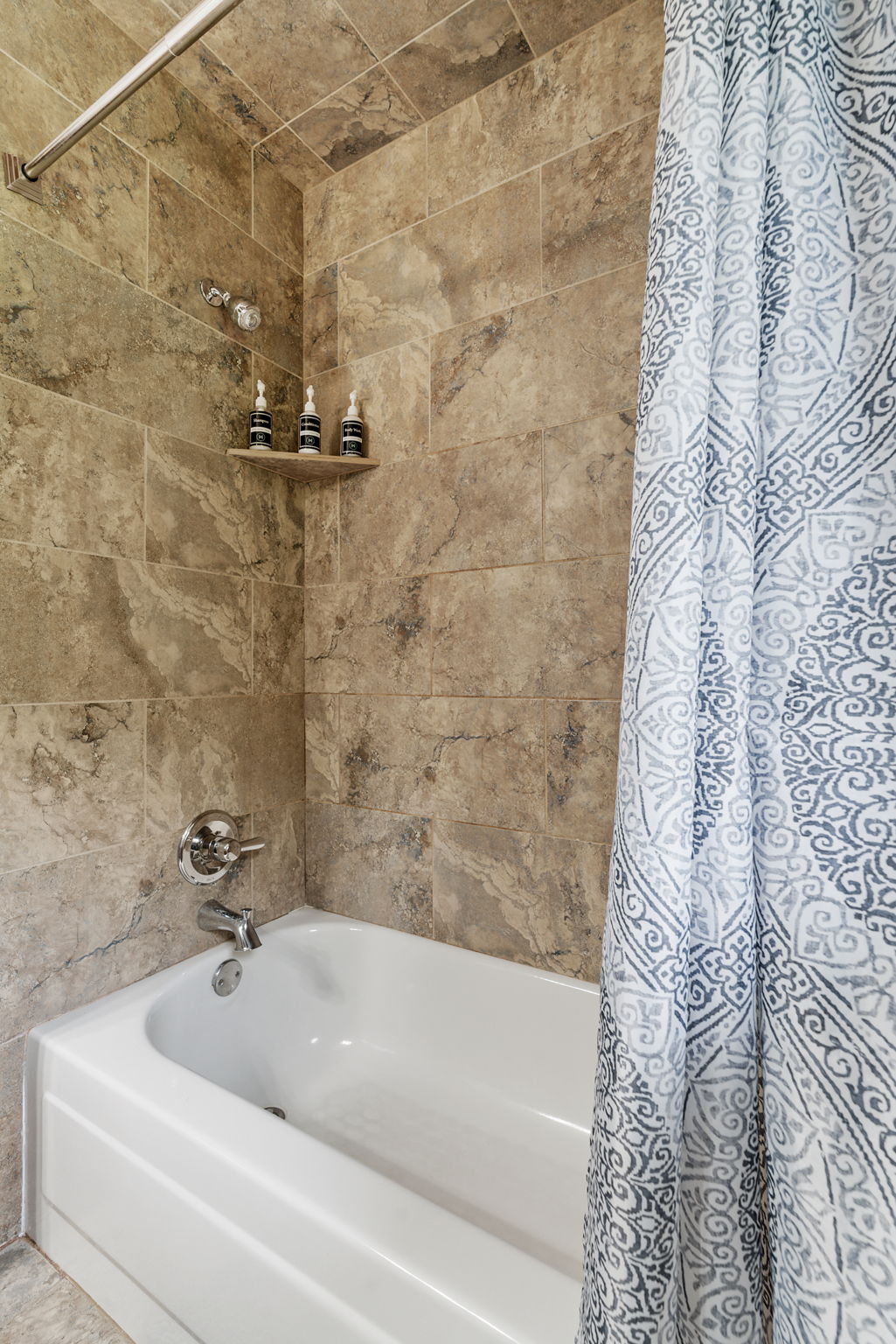 A modern bathroom featuring a beige tiled bathtub area with a patterned shower curtain.