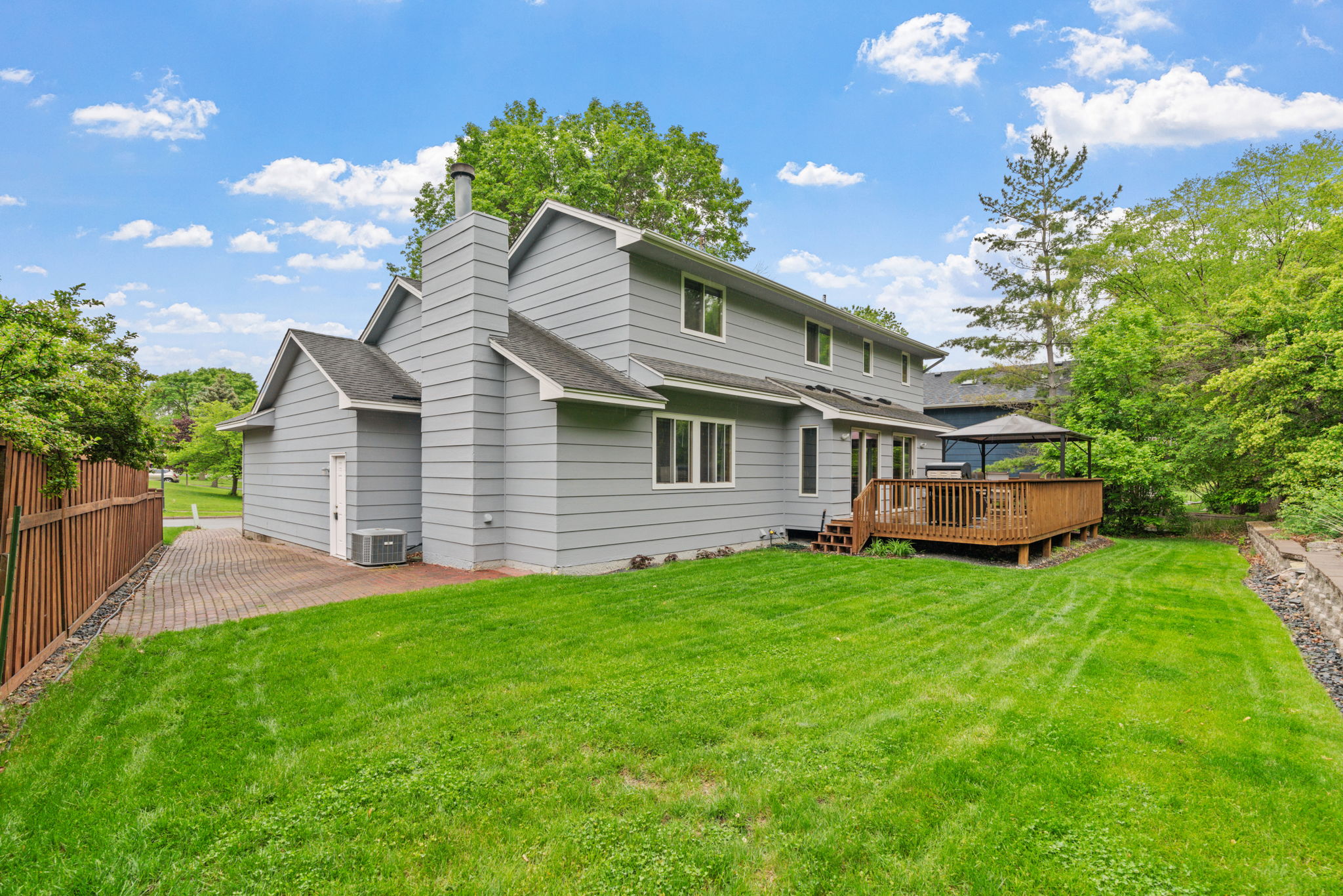 A charming gray house with a wooden deck and lush lawn under a blue sky.