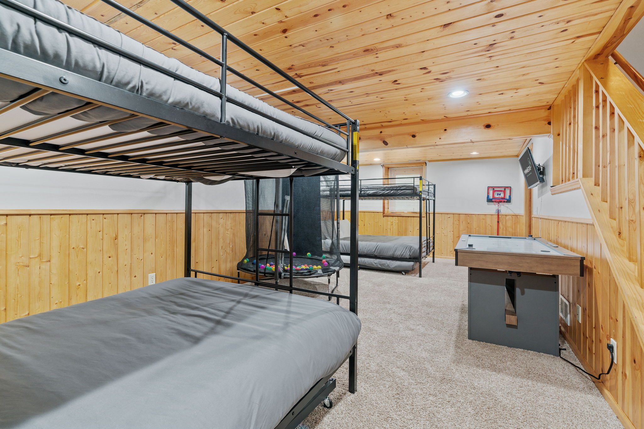 A cozy basement bedroom featuring bunk beds, a trampoline, and an air hockey table.