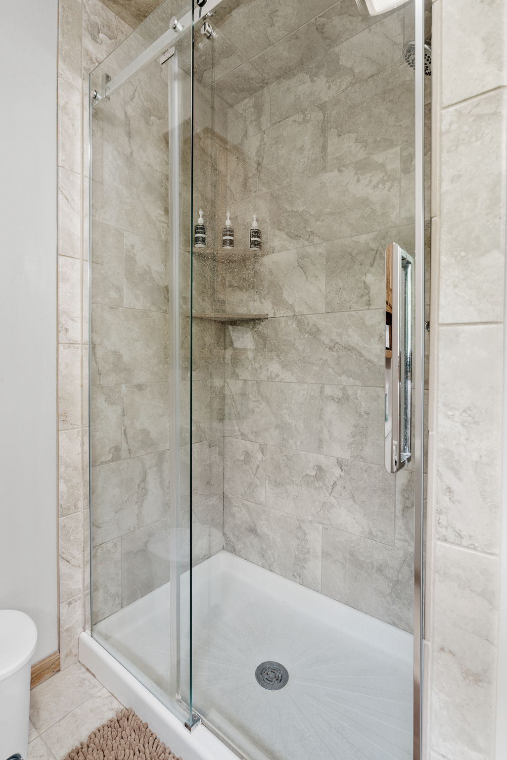 A modern shower enclosure featuring glass doors and gray tiled walls.